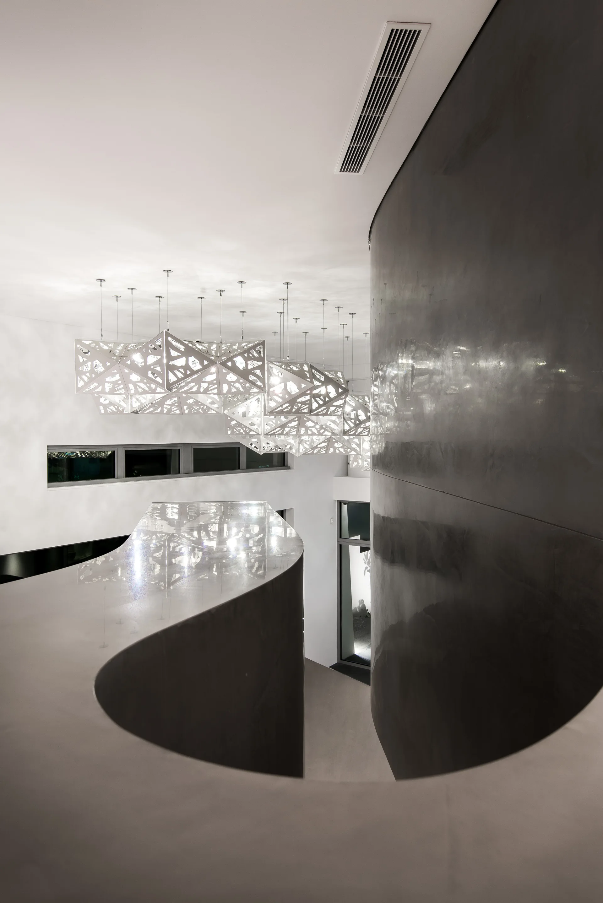A contemporary staircase features a sweeping curved dark grey wall and a large cluster of white geometric lattice pendant lights hanging from a white ceiling.