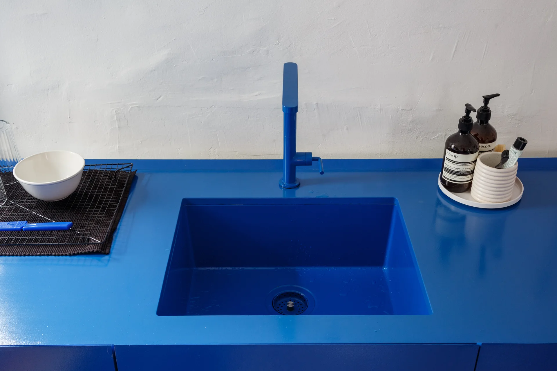 A close-up of a vibrant blue integrated sink and faucet set in a matching blue countertop against a textured white plaster wall.