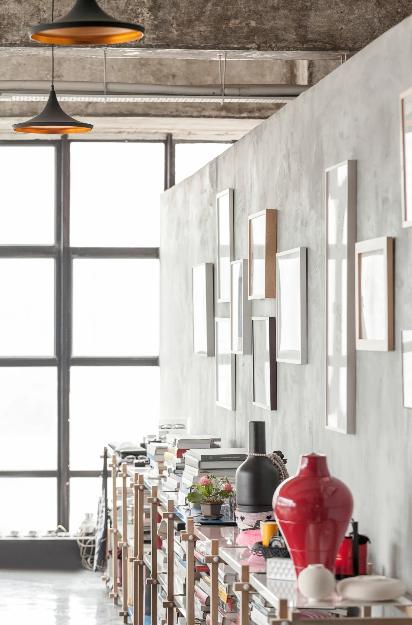 An industrial loft interior featuring a textured concrete wall decorated with framed art, sitting behind a low wood shelving unit.