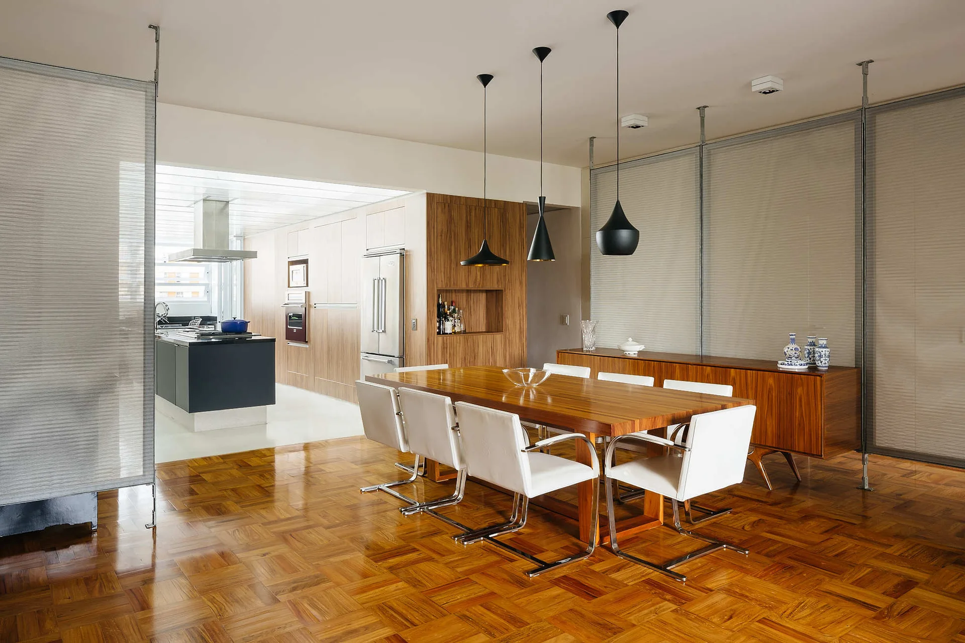 A contemporary dining room featuring a wood table with white chairs on parquet flooring, partitioned by translucent floor-to-ceiling screens.