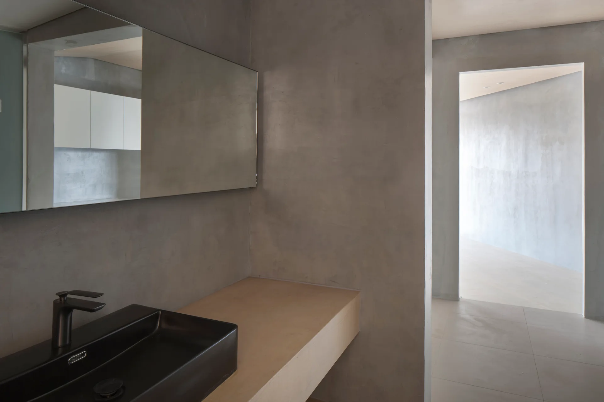 A modern bathroom showcases a black rectangular sink on a light wood floating vanity counter against smooth gray concrete walls.