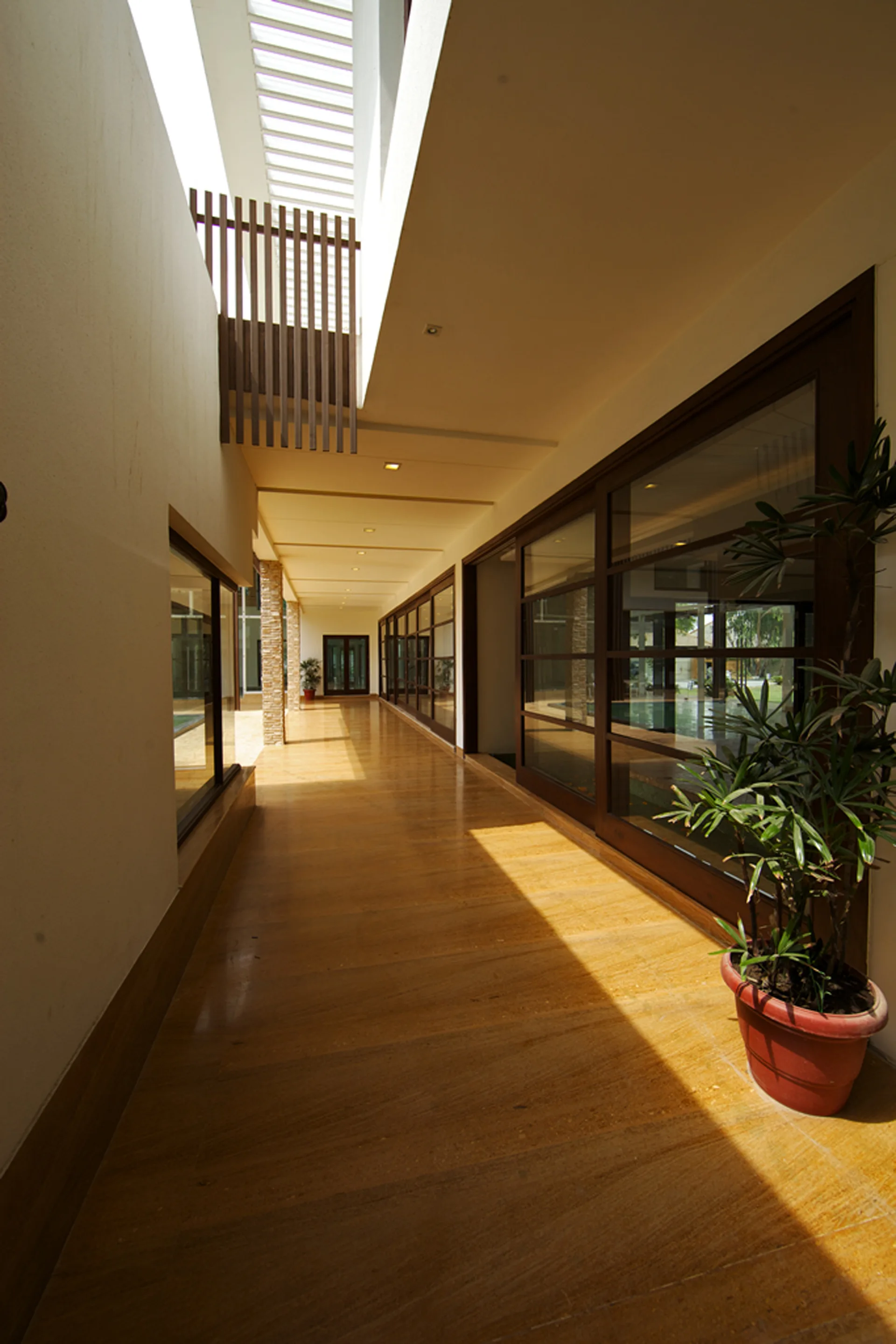 A long, sunlit indoor hallway features polished wood flooring, glass-paneled walls, and a linear skylight overhead.