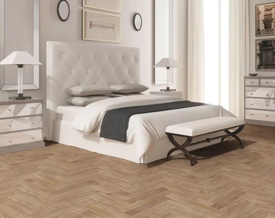 A symmetrical bedroom featuring a white tufted headboard, mirrored bedside tables, table lamps, and light herringbone patterned wood flooring.