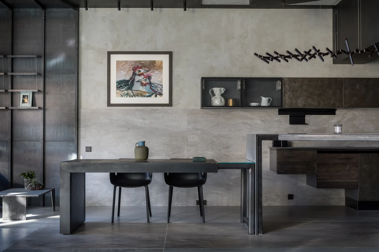 An industrial dining area features a dark metal table, matching chairs, and textured stone walls below mesh-front cabinetry.