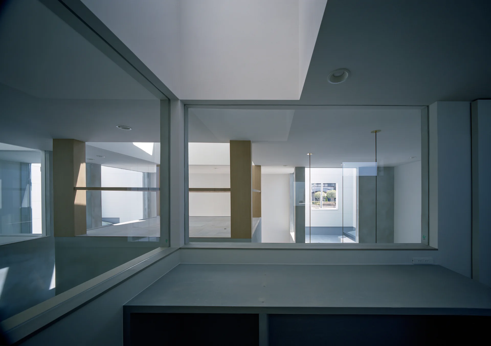 A minimalist multi-level interior features expansive glass partitions, light-toned wooden pillars, and recessed white ceilings with deep light wells.