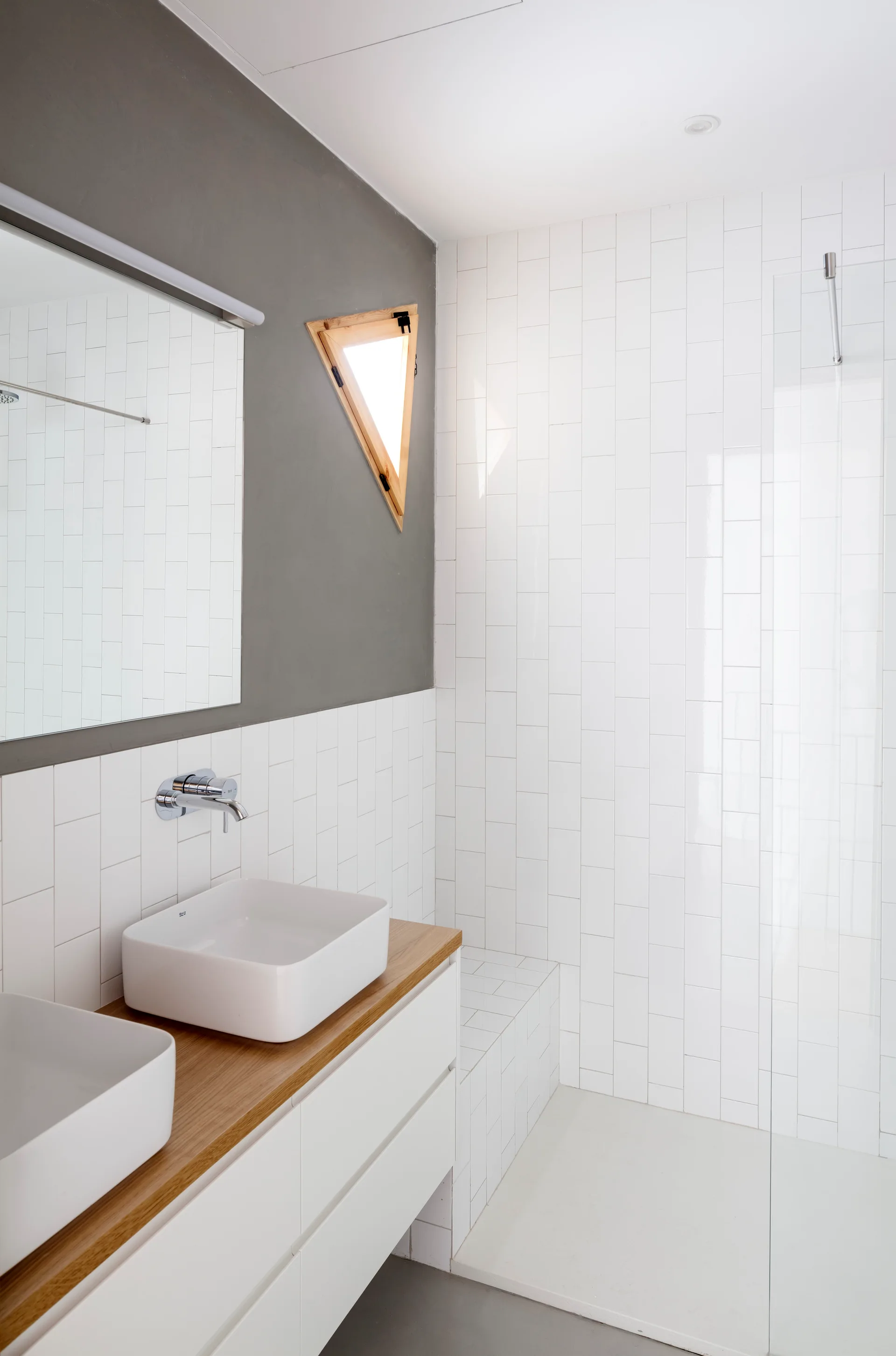A contemporary bathroom features a white double vanity with a wood countertop, vertically stacked white subway tiles, and a walk-in shower.