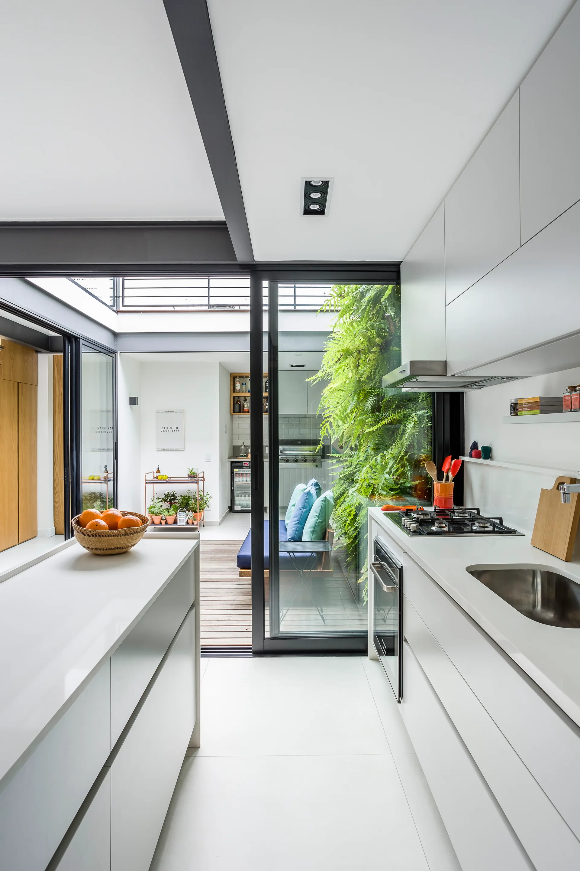 A modern white galley kitchen features flat-front cabinets and a sliding glass door opening to a patio with a lush green vertical garden.
