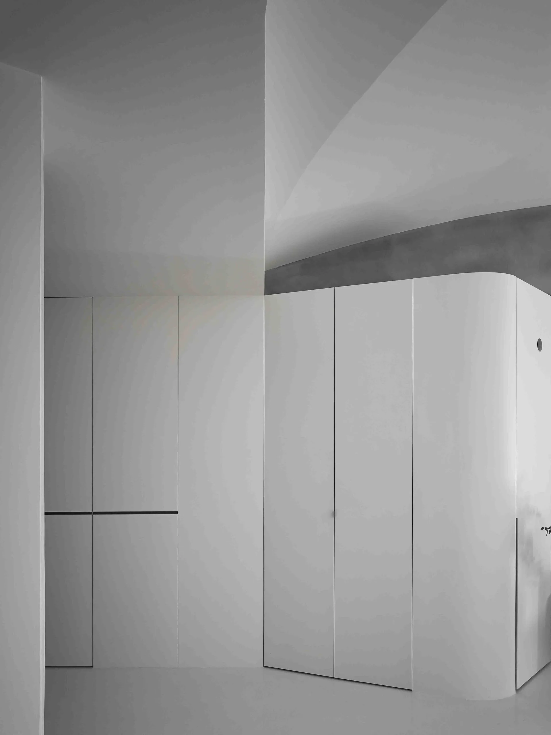 Seamless matte white built-in cabinetry featuring a rounded corner stands in a minimalist hallway under soft ambient lighting.