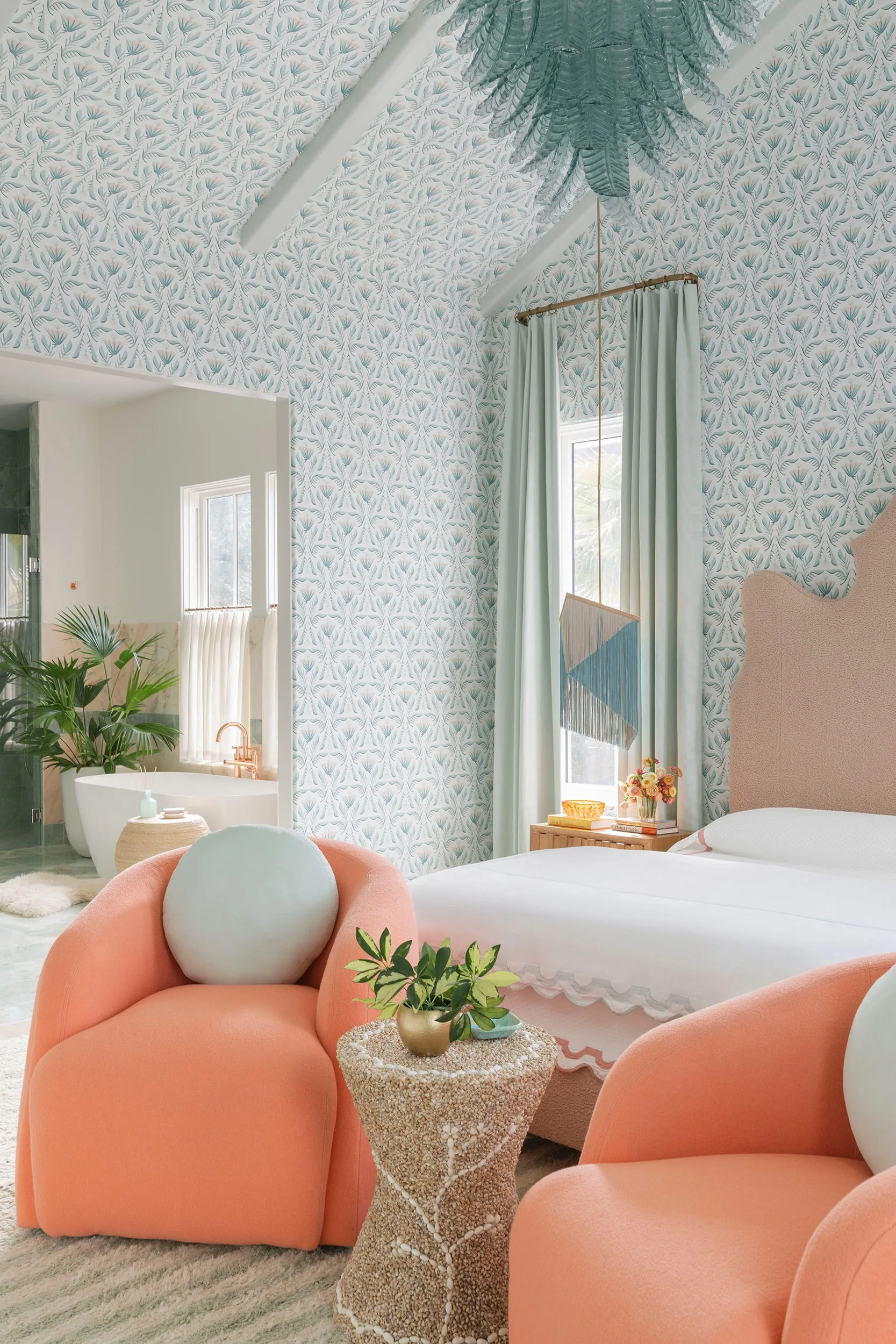 A pastel bedroom features mint green botanical wallpaper on the walls and ceiling, peach armchairs, and a bed with a scalloped pink headboard.