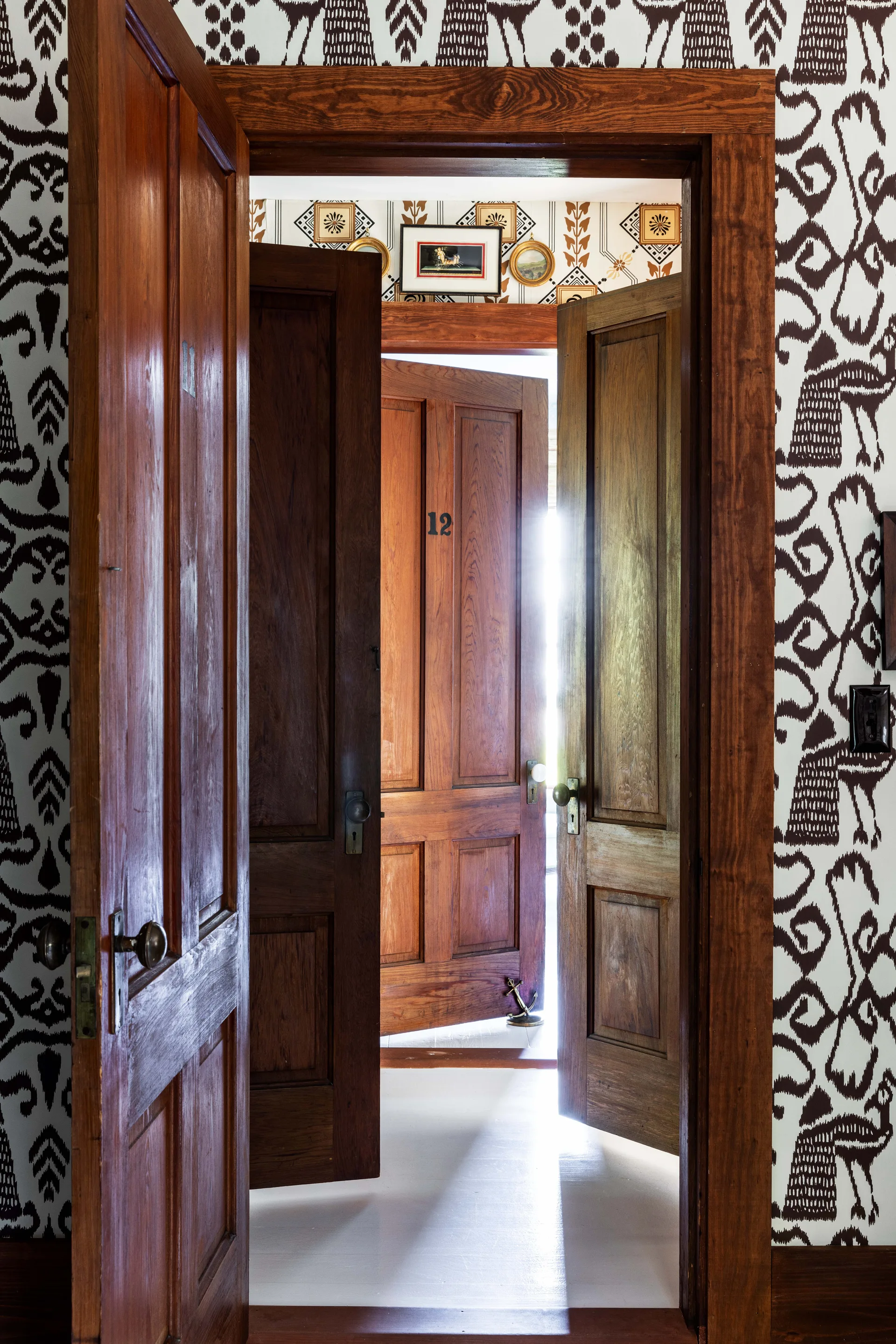 A view through successive open wooden doors in a hallway featuring bold brown and white patterned wallpaper and light-colored floors.