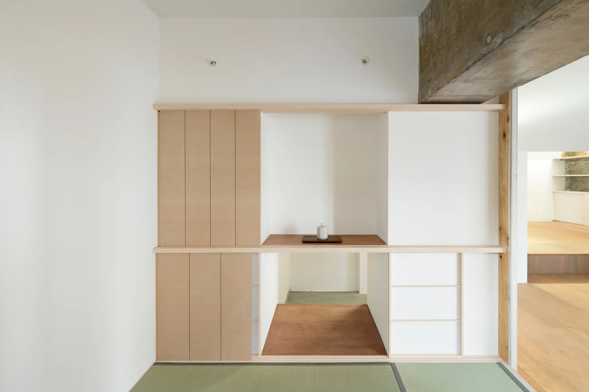 A minimalist room featuring custom built-in wooden cabinetry with sliding panels, a central recessed alcove, and green tatami floor mats.