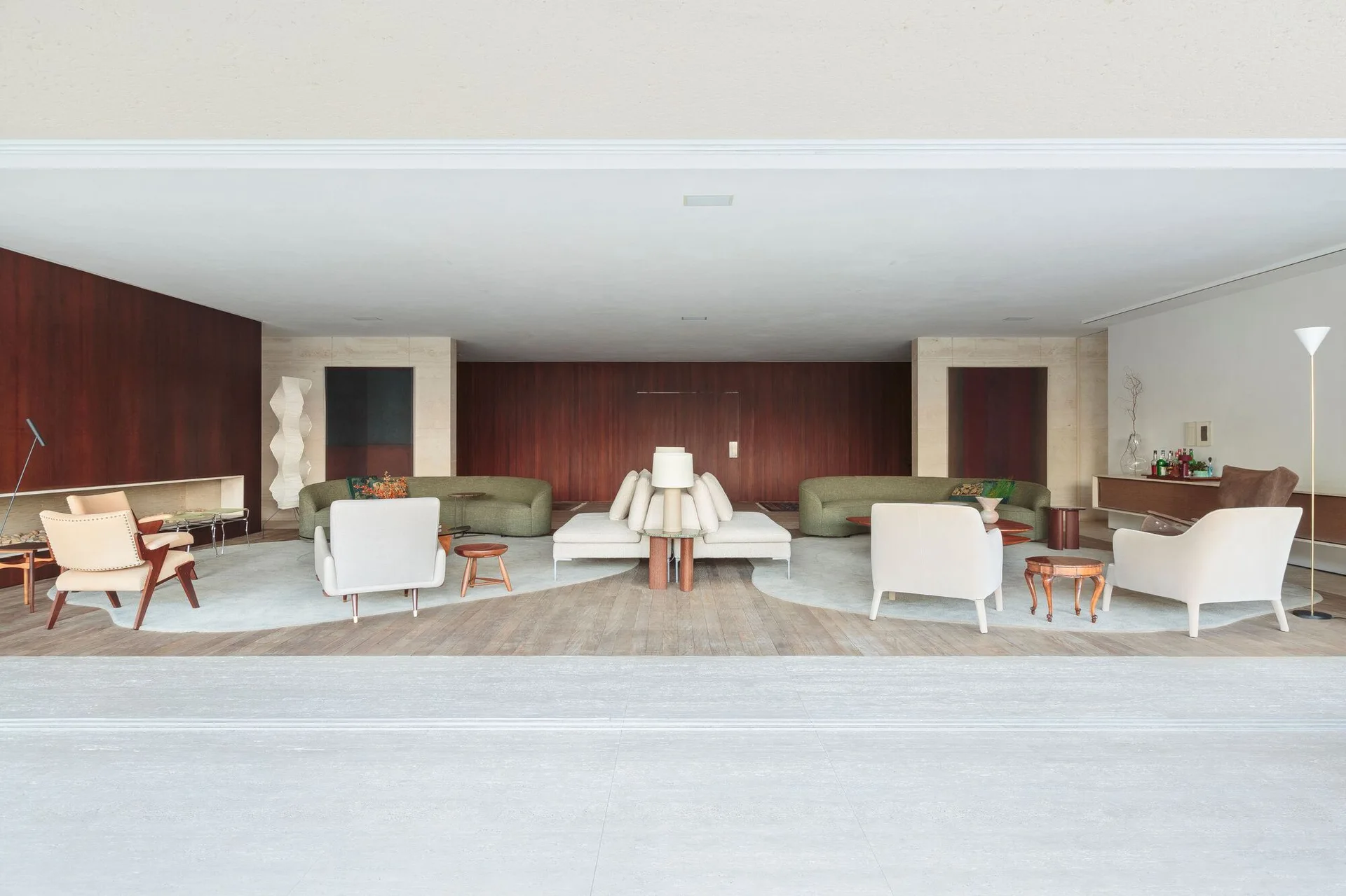 A spacious mid-century modern living room featuring curved olive green sofas, light armchairs, and a central back-to-back sectional on shaped rugs.