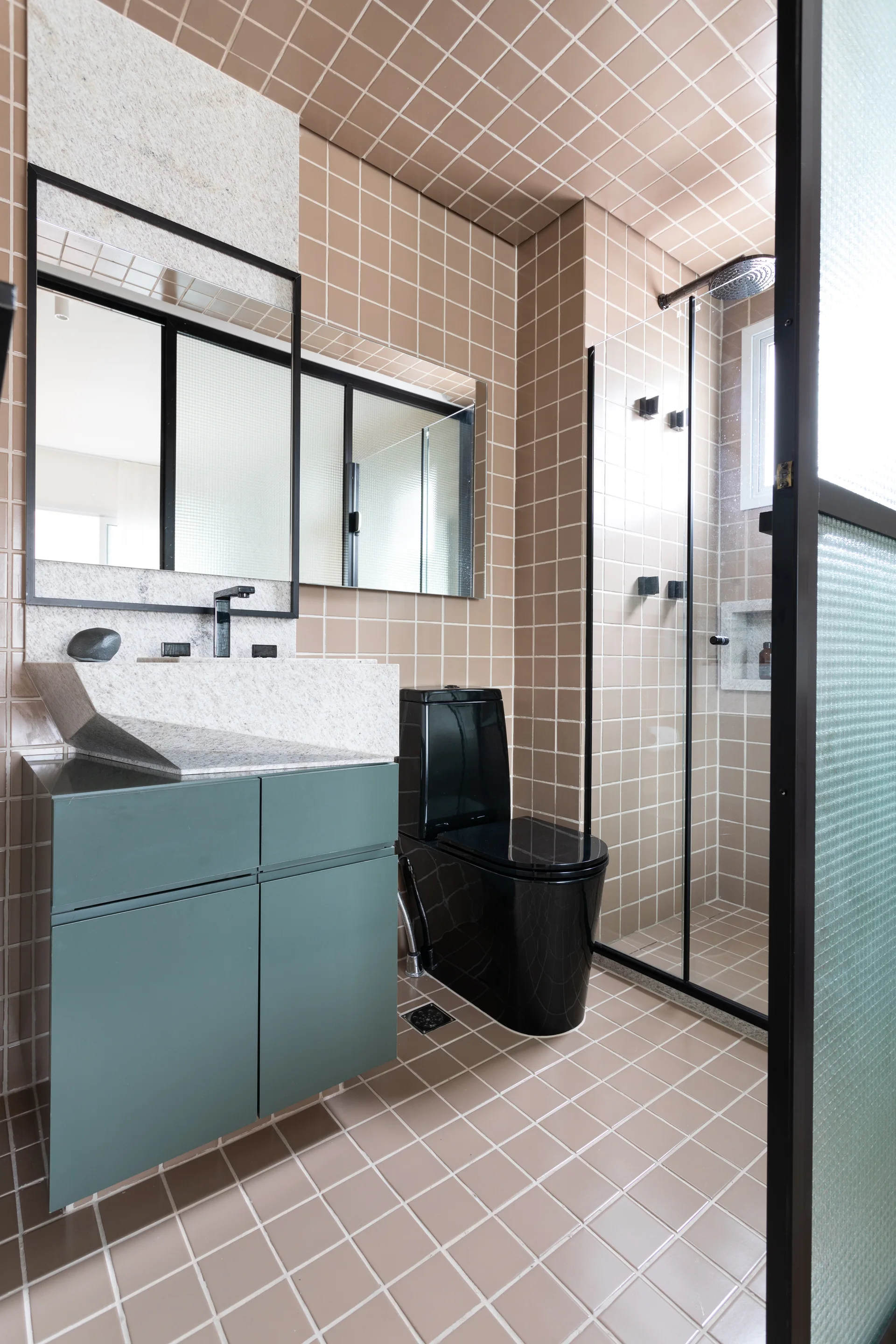 A modern bathroom features beige grid-tiled walls and ceiling, a sage green vanity with a stone sink, a black toilet, and a glass shower enclosure.