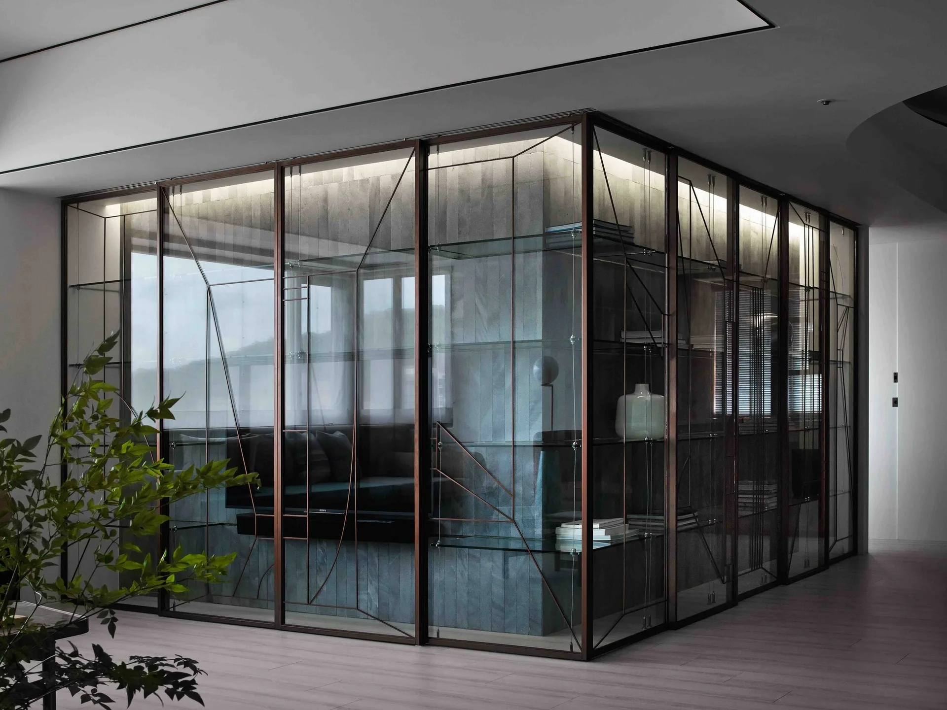 A modern corner glass partition with bronze framing showcases glass shelving against a textured grey stone wall.