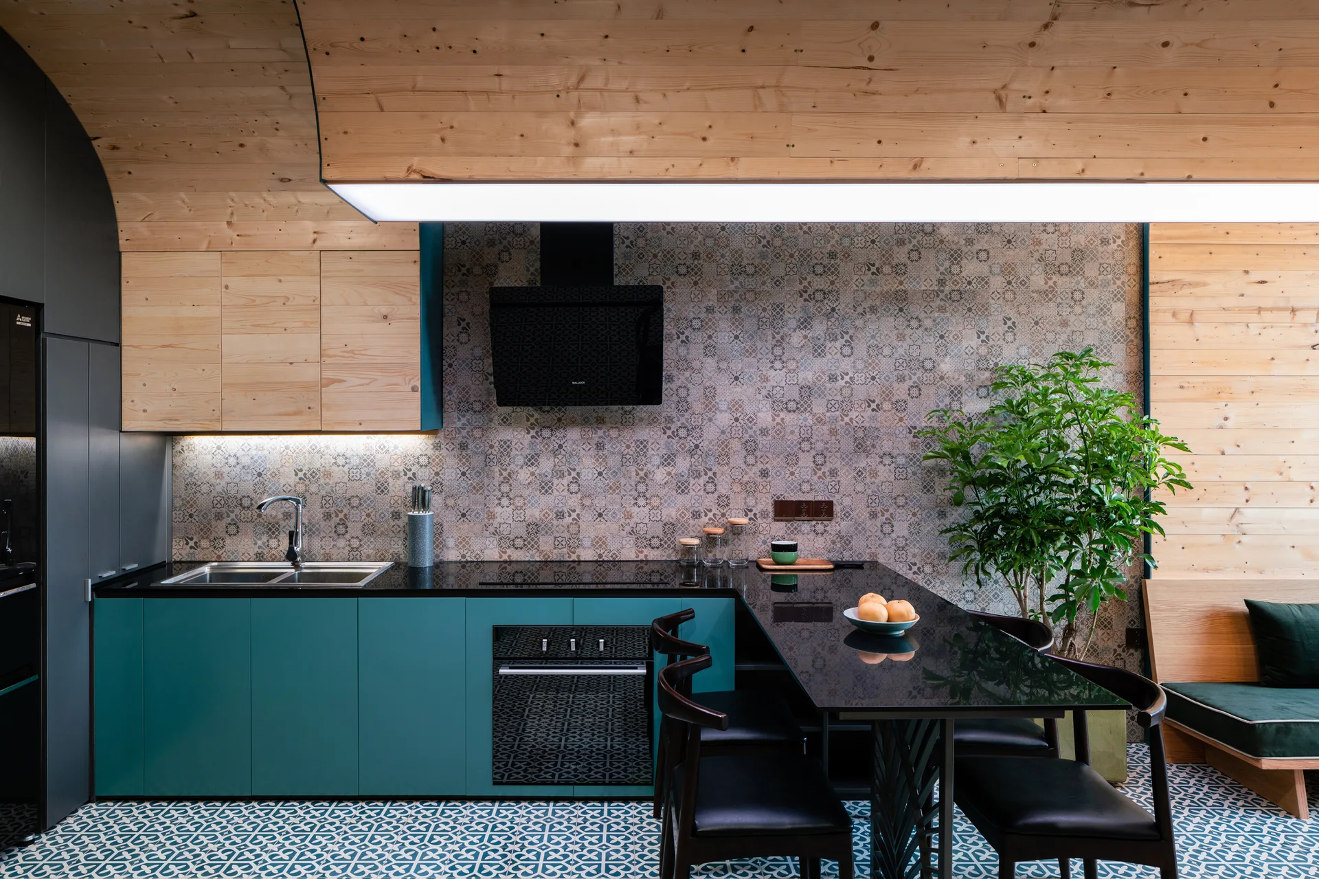 A modern kitchen featuring teal lower cabinets, patterned tile walls, a black countertop dining table, and a curved light wood paneled ceiling.