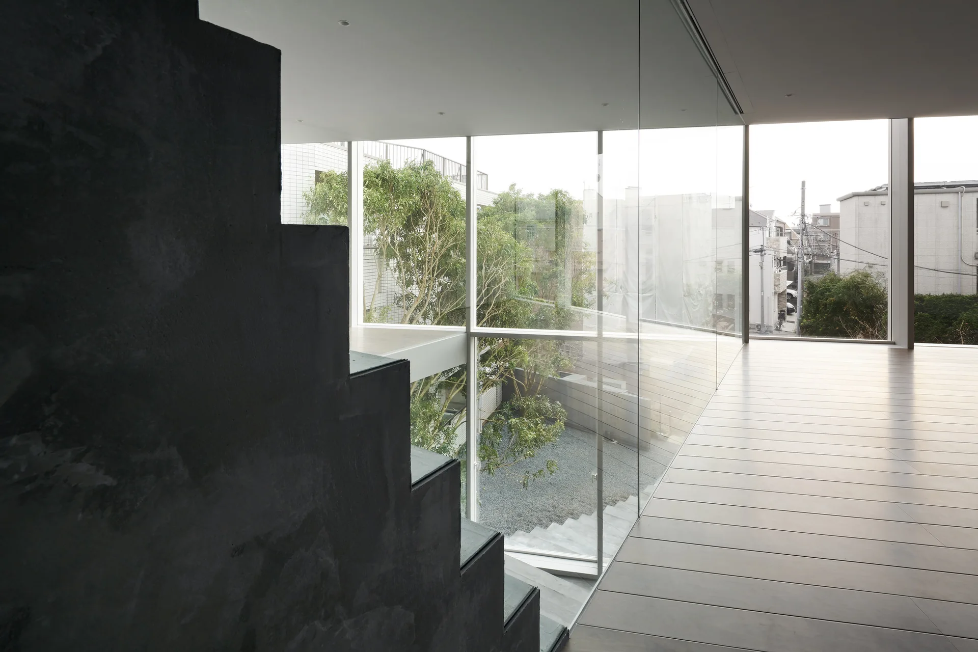 A dark textured sculptural staircase stands beside a large glass wall showcasing an outdoor courtyard with green trees.