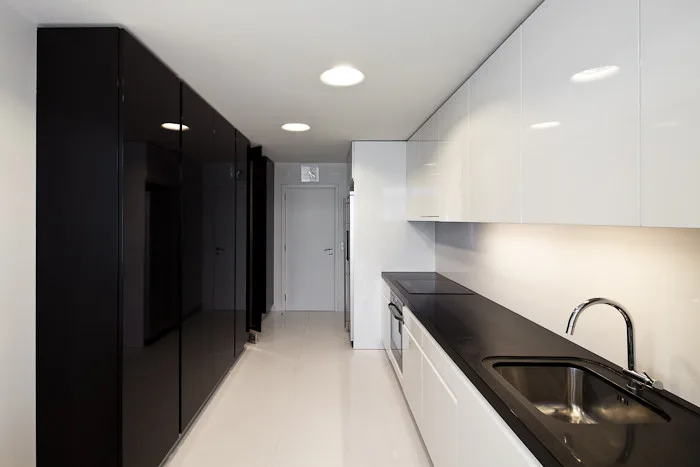 A minimalist galley kitchen features high-gloss black cabinets on one wall and white cabinets with a black countertop and built-in sink on the other.