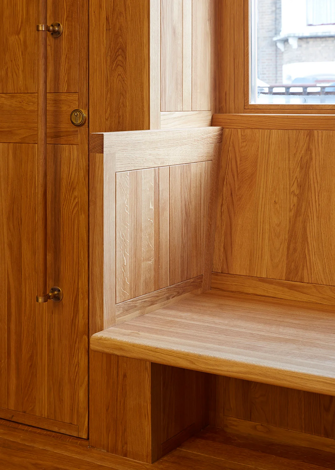 A close-up of custom oak built-in cabinetry featuring an integrated wooden bench, vertical wood paneling, and a door with metal handles.