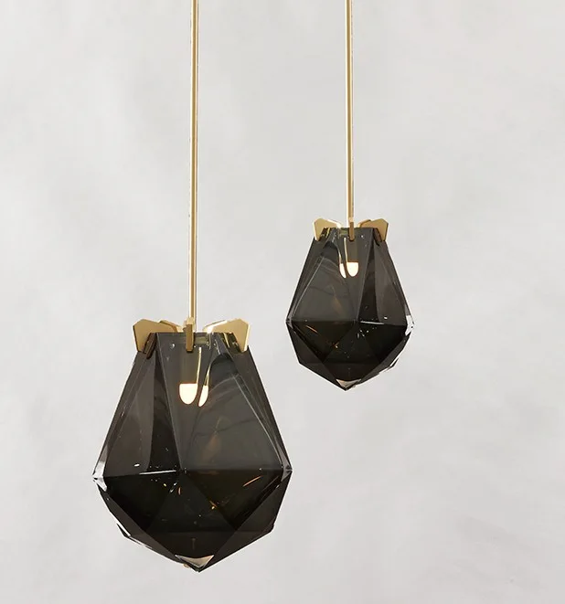 Two faceted smoky glass pendant lights with gold hardware hang at staggered heights against a plain light gray background.