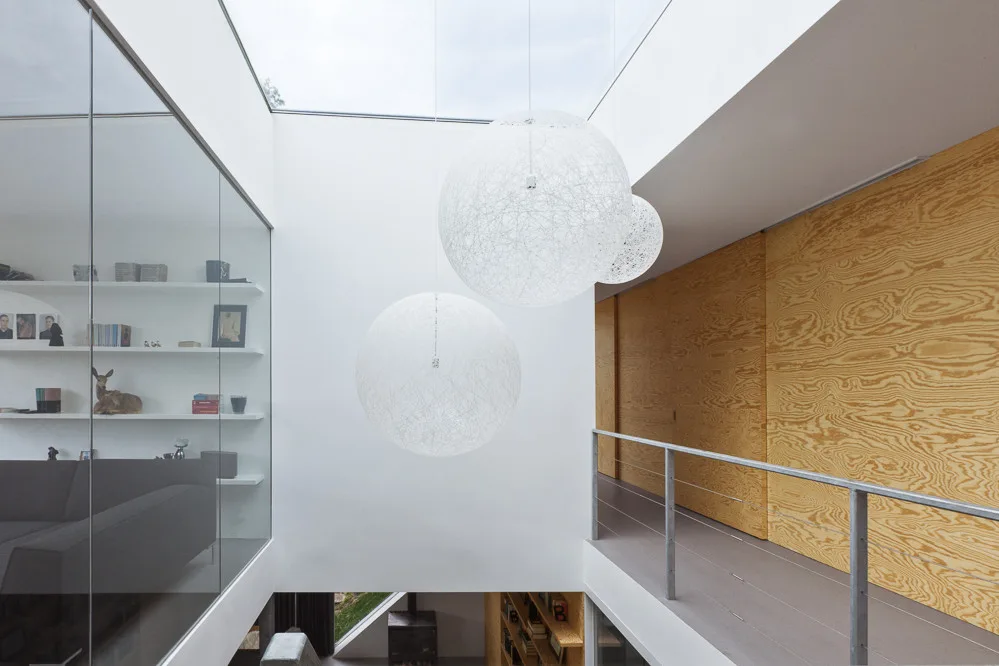 A modern mezzanine landing features large white spherical pendant lights hanging below a skylight, with a plywood wall and glass partition.