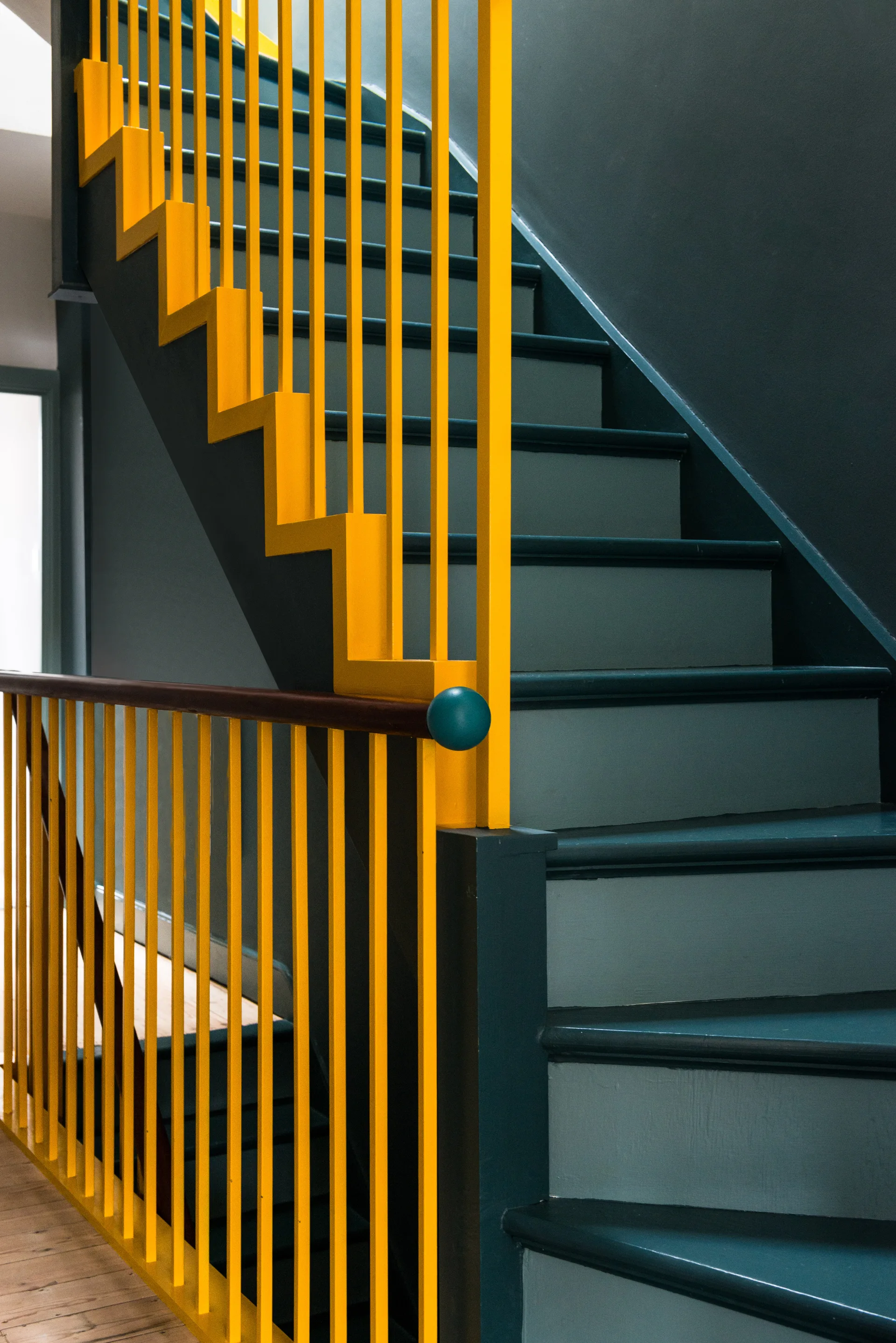 A modern interior staircase with dark teal painted walls and wood steps features a contrasting bright yellow metal geometric railing.