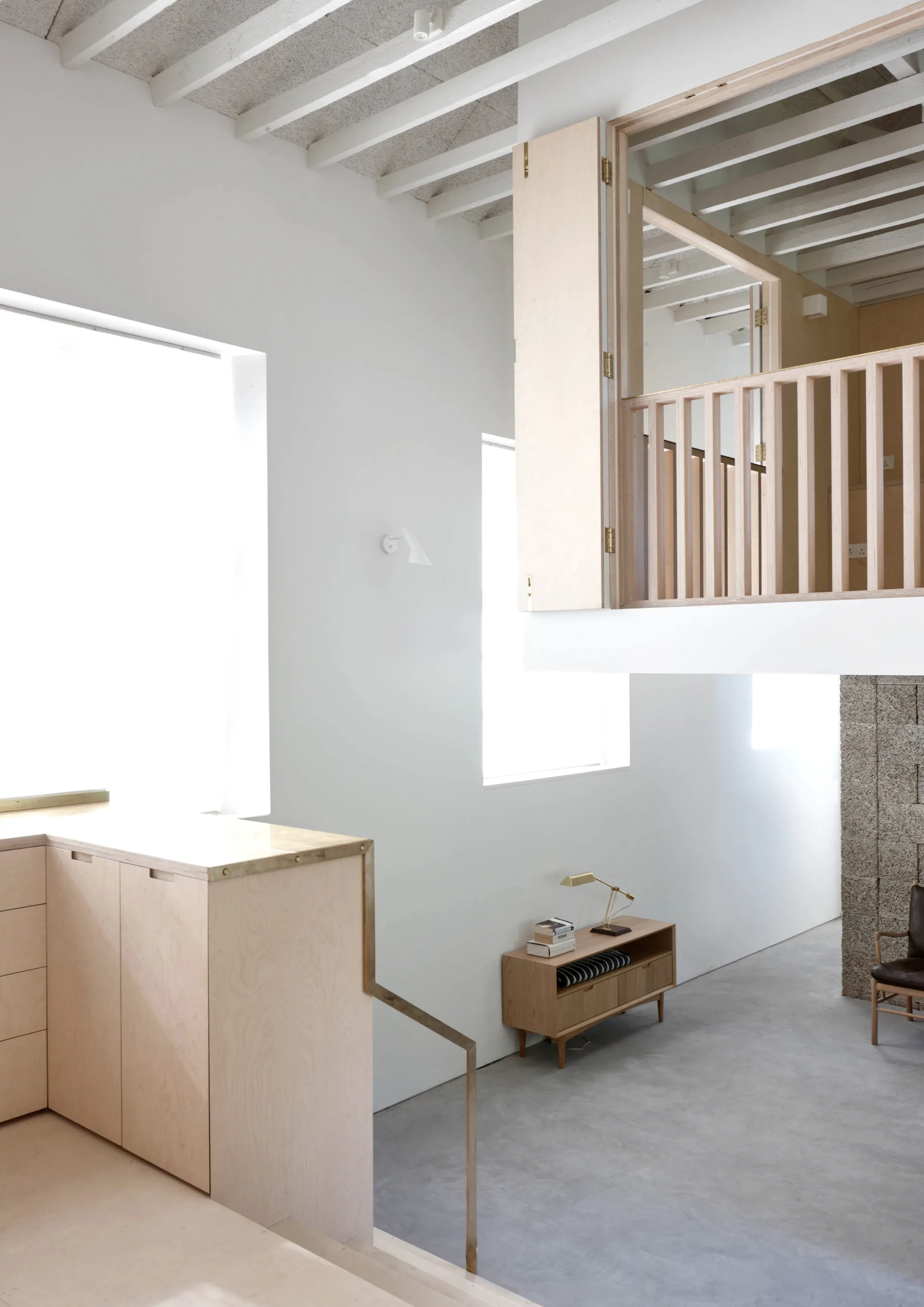 Minimalist double-height room featuring a light plywood mezzanine, white painted ceiling joists, concrete floors, and built-in cabinets.