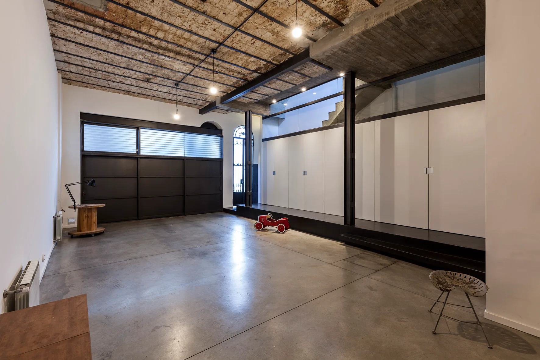 An industrial loft space featuring an exposed brick barrel vault ceiling, polished concrete floors, and a long wall of built-in white cabinets.