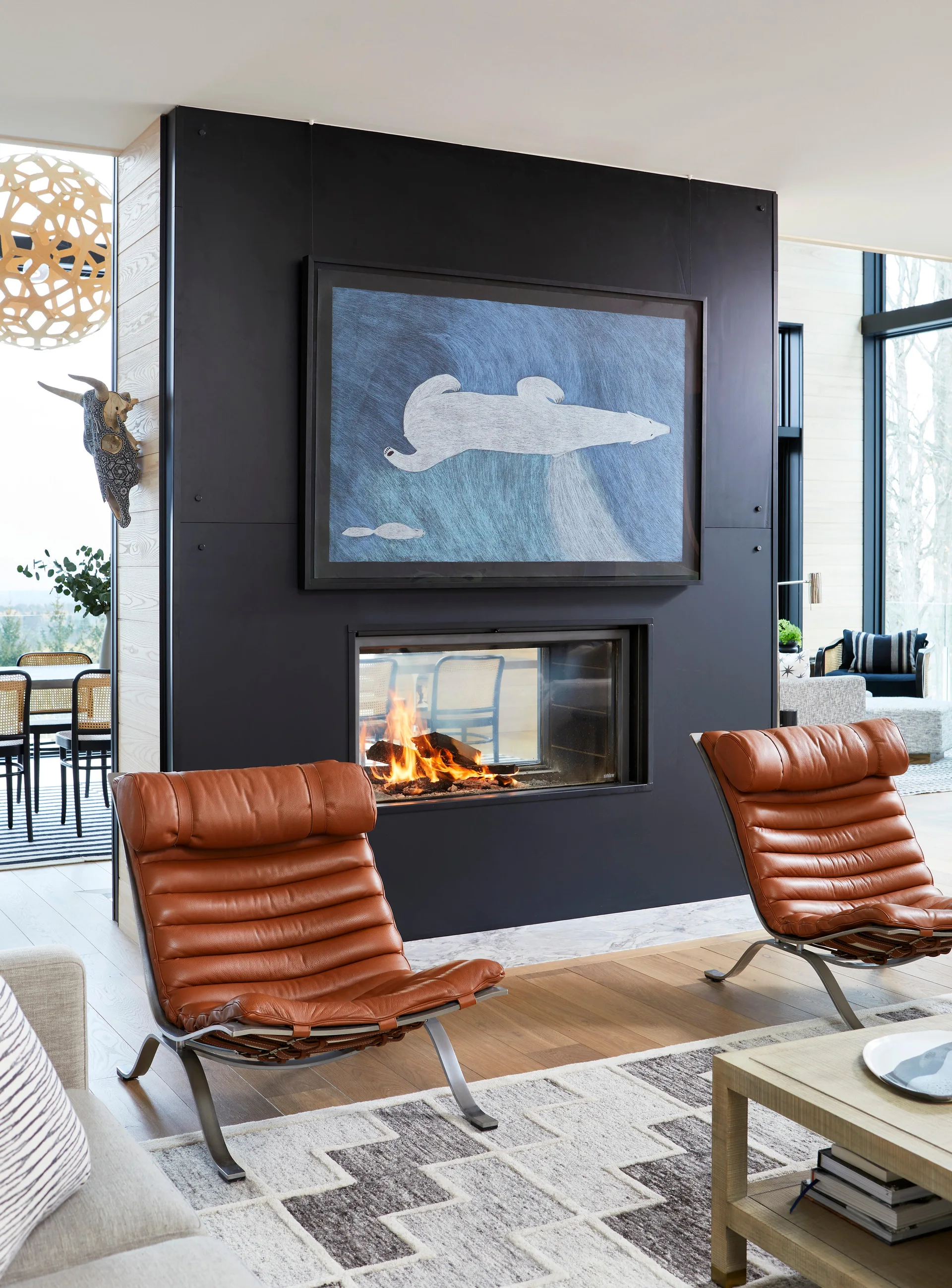 Two cognac leather lounge chairs sit before a double-sided fireplace built into a matte black partition wall decorated with blue polar bear art.