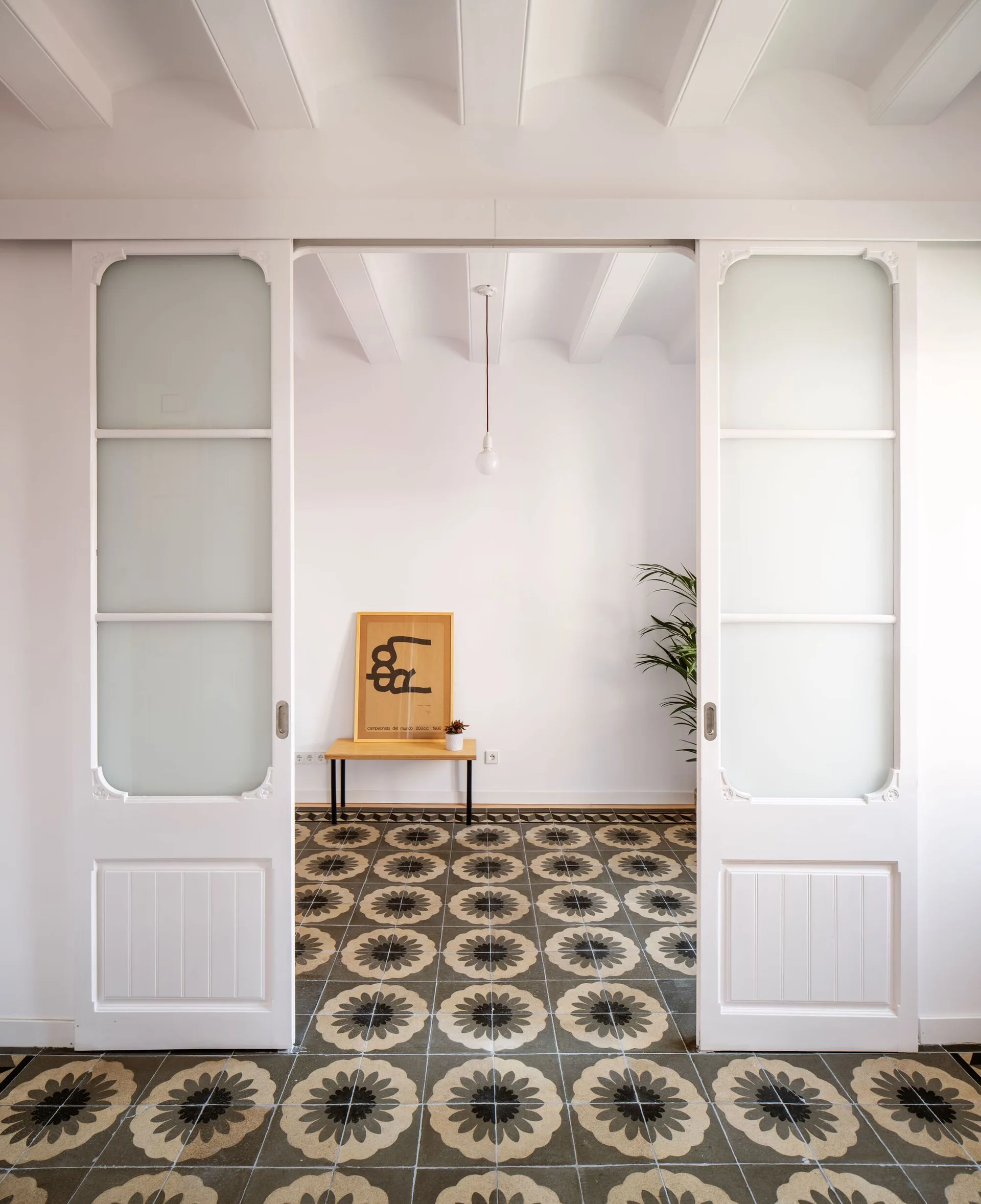 A view through frosted-glass sliding doors into a minimalist hallway featuring black and grey patterned floor tiles and a wood bench.