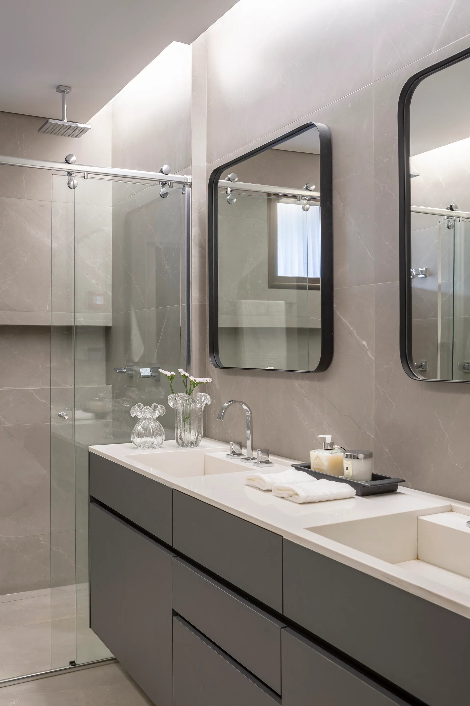 A modern bathroom features a charcoal floating vanity with integrated double sinks, thin black-framed mirrors, and grey marble-look tile walls.