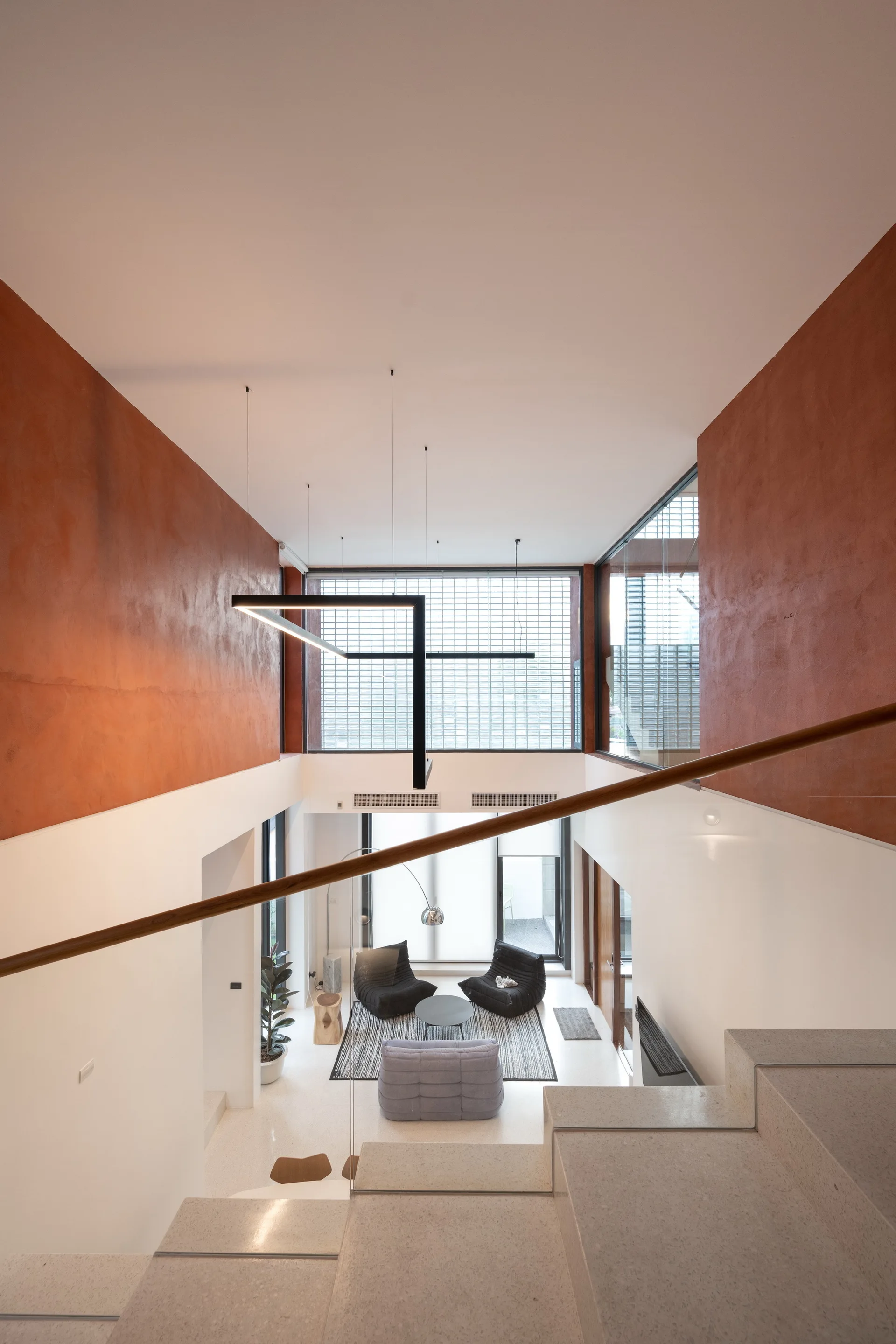High-angle view from a stone staircase looking down at a modern living room with rust-orange plaster walls, low-profile seating, and a glass block wall.