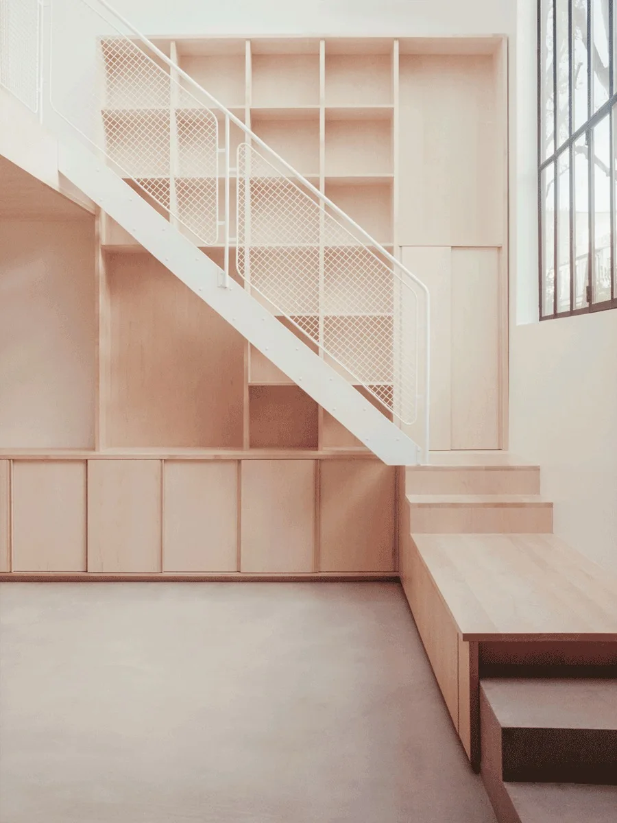 A minimalist interior featuring a light wood staircase integrated with a built-in storage unit and a white mesh metal railing.
