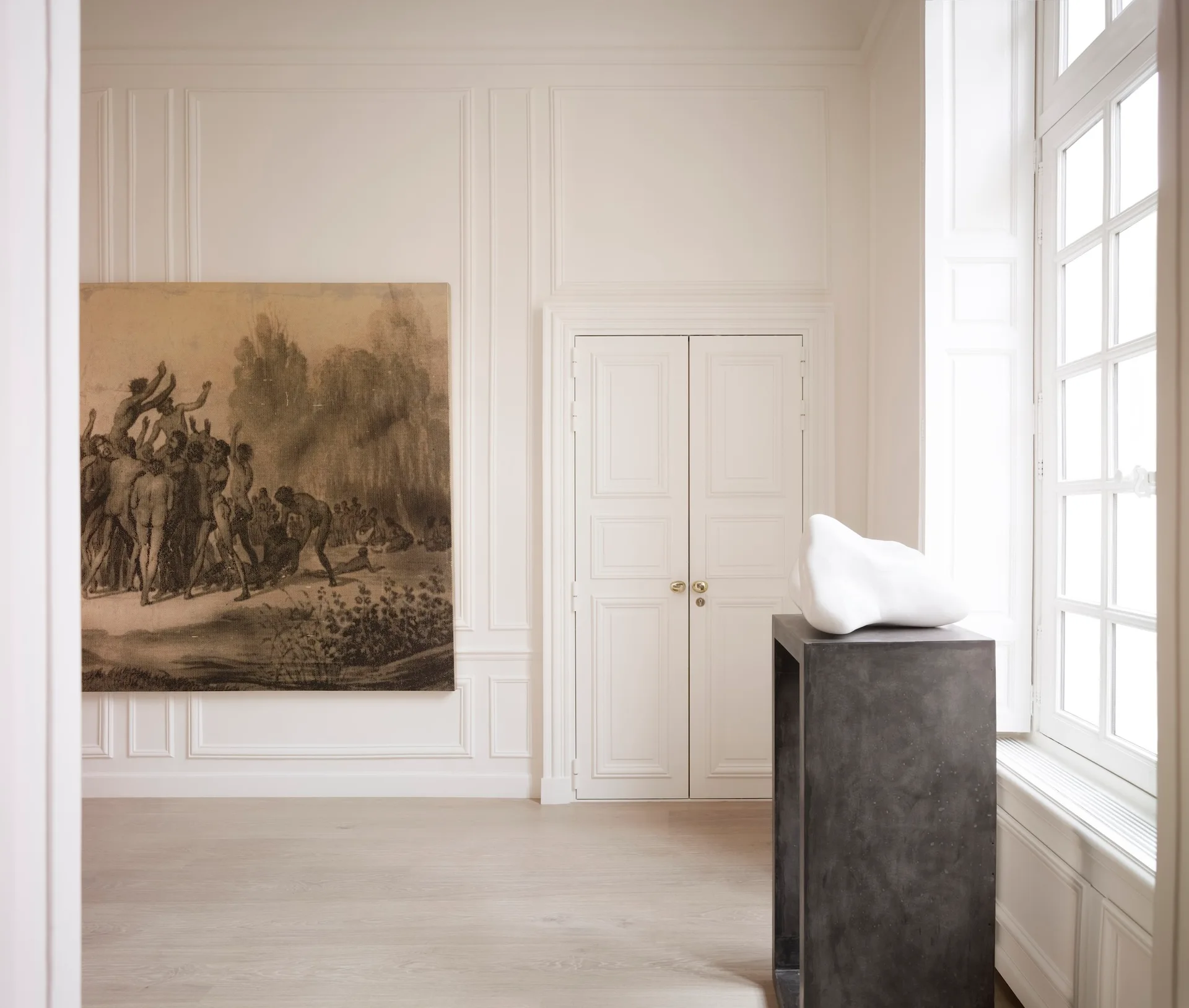 A minimalist room featuring white paneled walls, a large monochrome drawing, a double door, and a white sculpture on a dark gray pedestal.