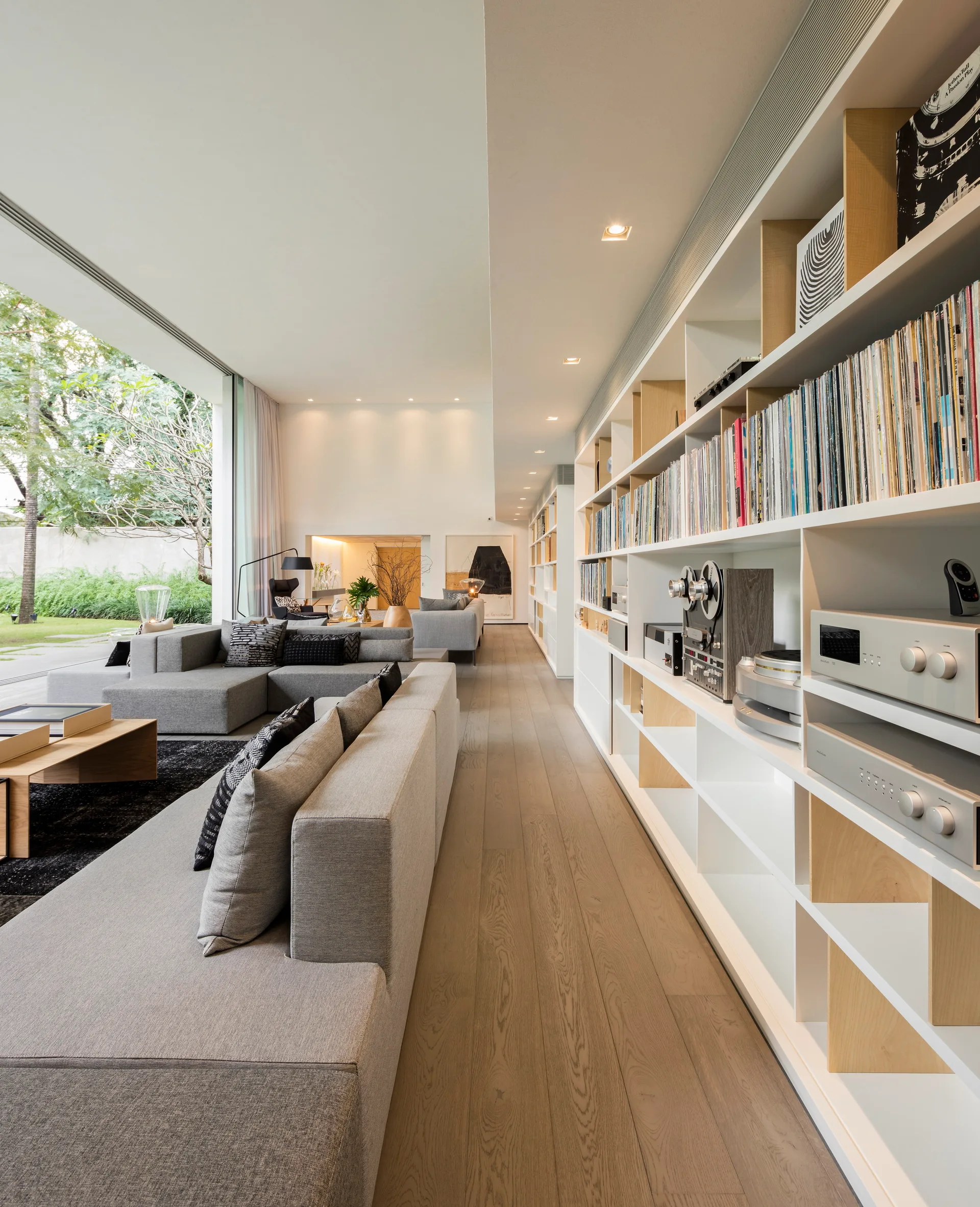 A modern living room with a grey sectional sofa, light wood floors, and a long built-in bookcase filled with vinyl records and audio gear.
