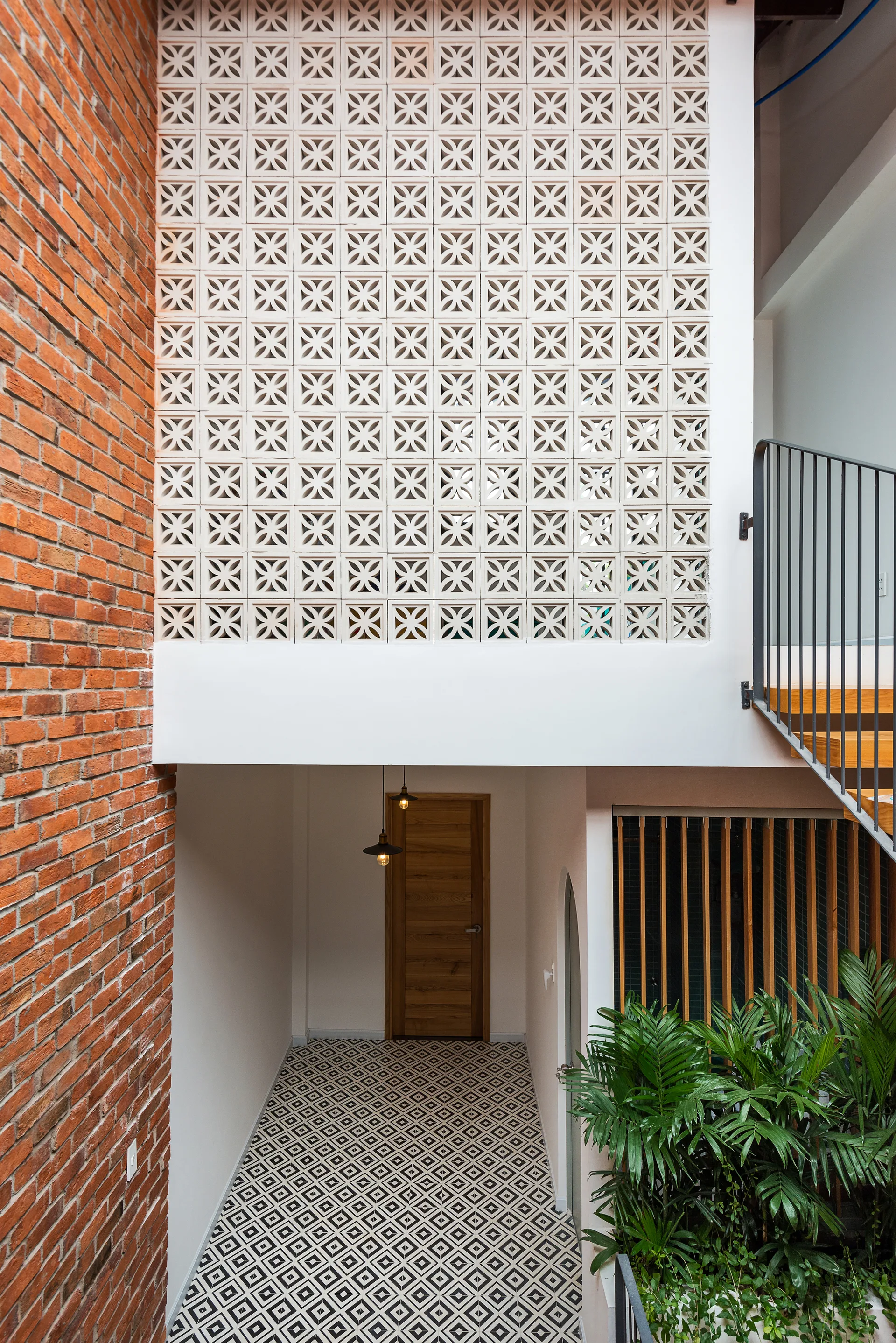 A multi-level hallway featuring a black and white geometric tiled floor, an exposed red brick wall, and a large white breeze block screen.