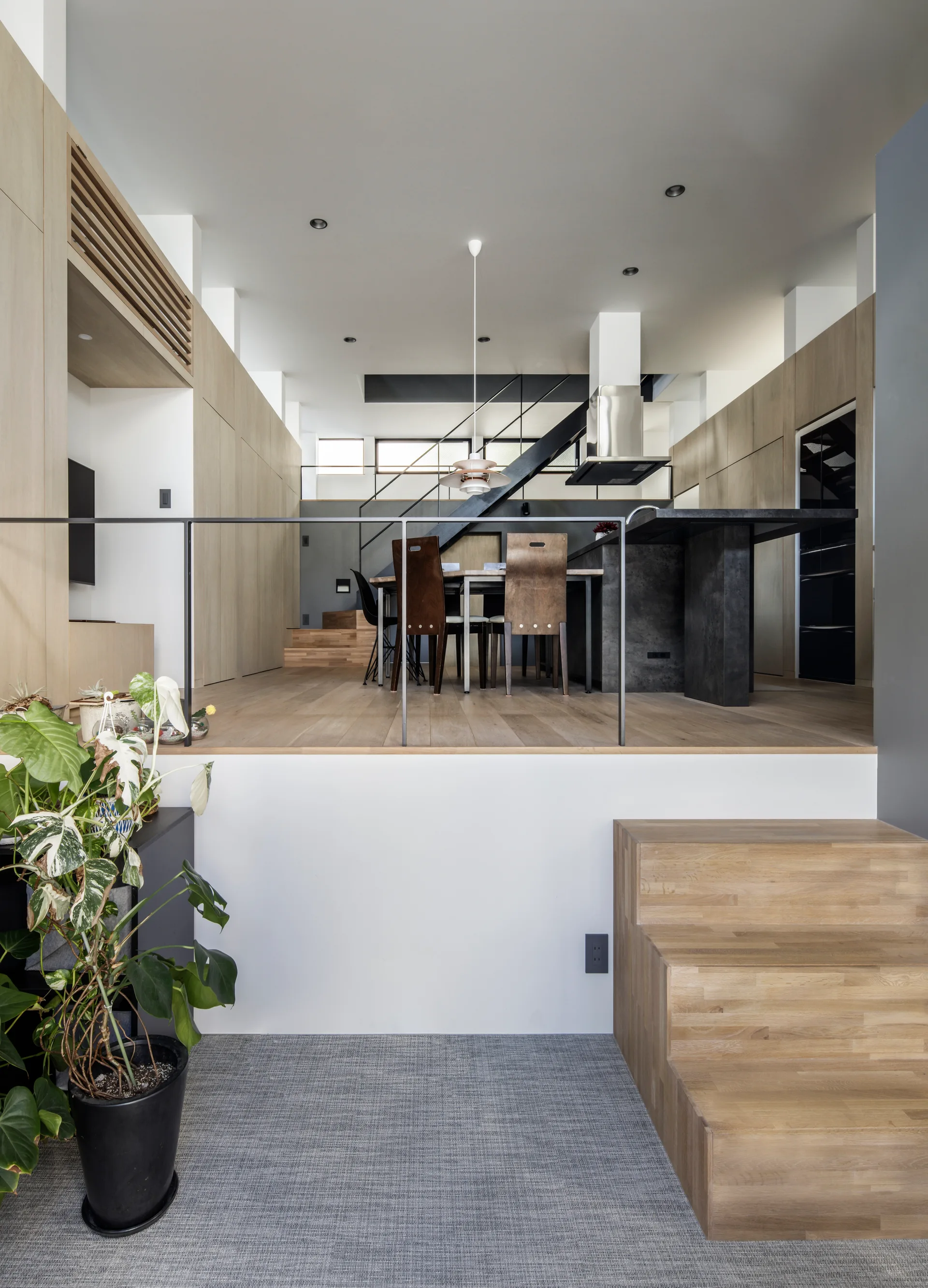 A modern split-level interior features a raised kitchen and dining area with extensive wood cabinetry, a dark island, and a black steel staircase.