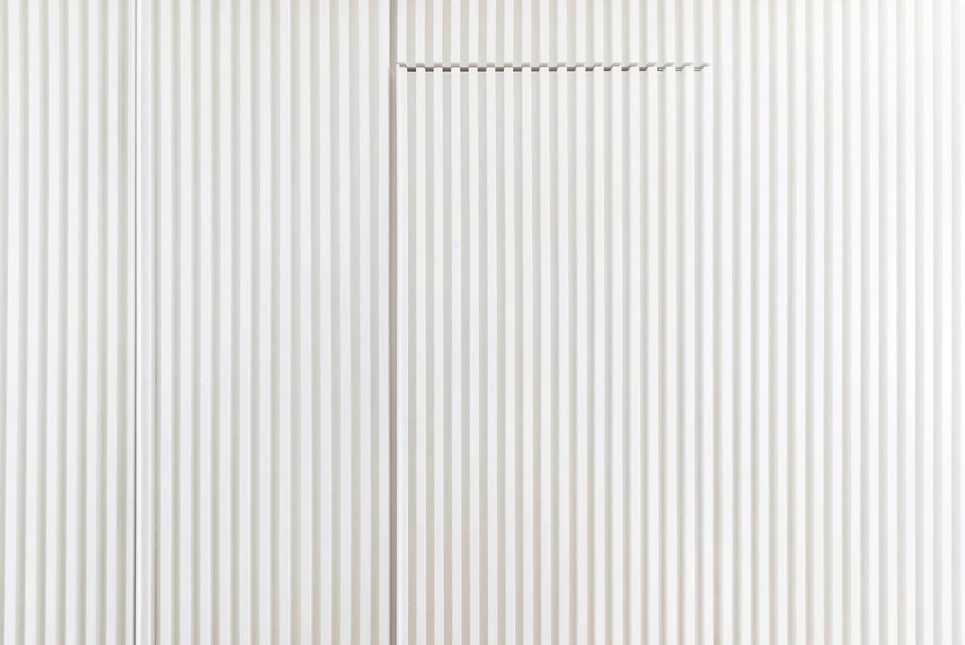 A close-up view of white vertical slat wall paneling featuring a seamless flush-mounted hidden door.