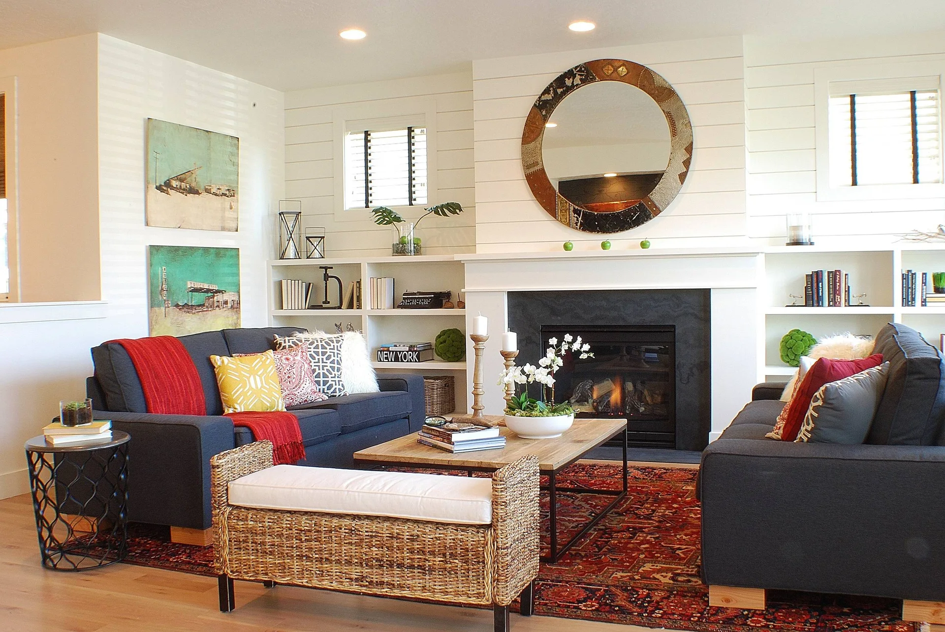 A symmetric living room features two dark gray sofas facing a white shiplap fireplace with built-in bookshelves and a red patterned rug.