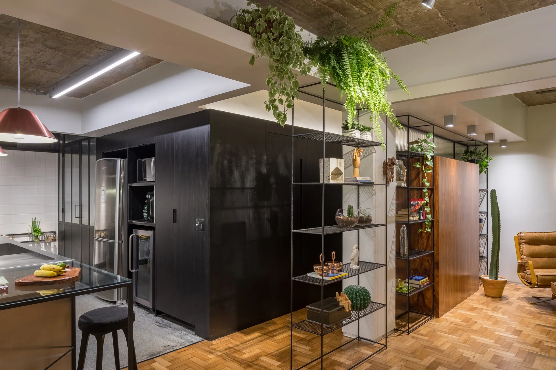 An open kitchen features dark wood-grained cabinets, a stainless steel refrigerator, tall wire shelving, and parquet flooring.