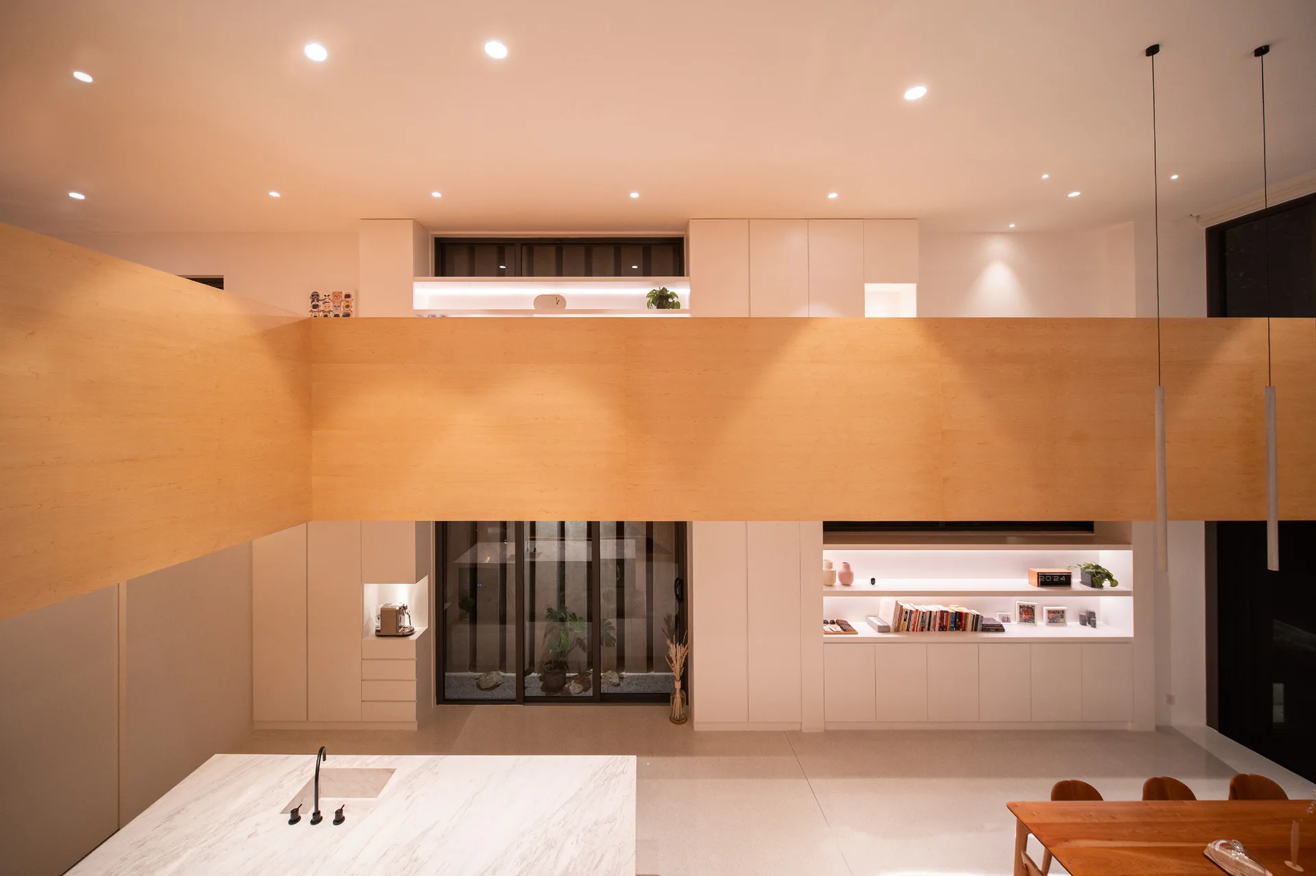 A minimalist kitchen featuring a marble island, white built-in cabinetry, and a prominent horizontal light wood mezzanine partition.
