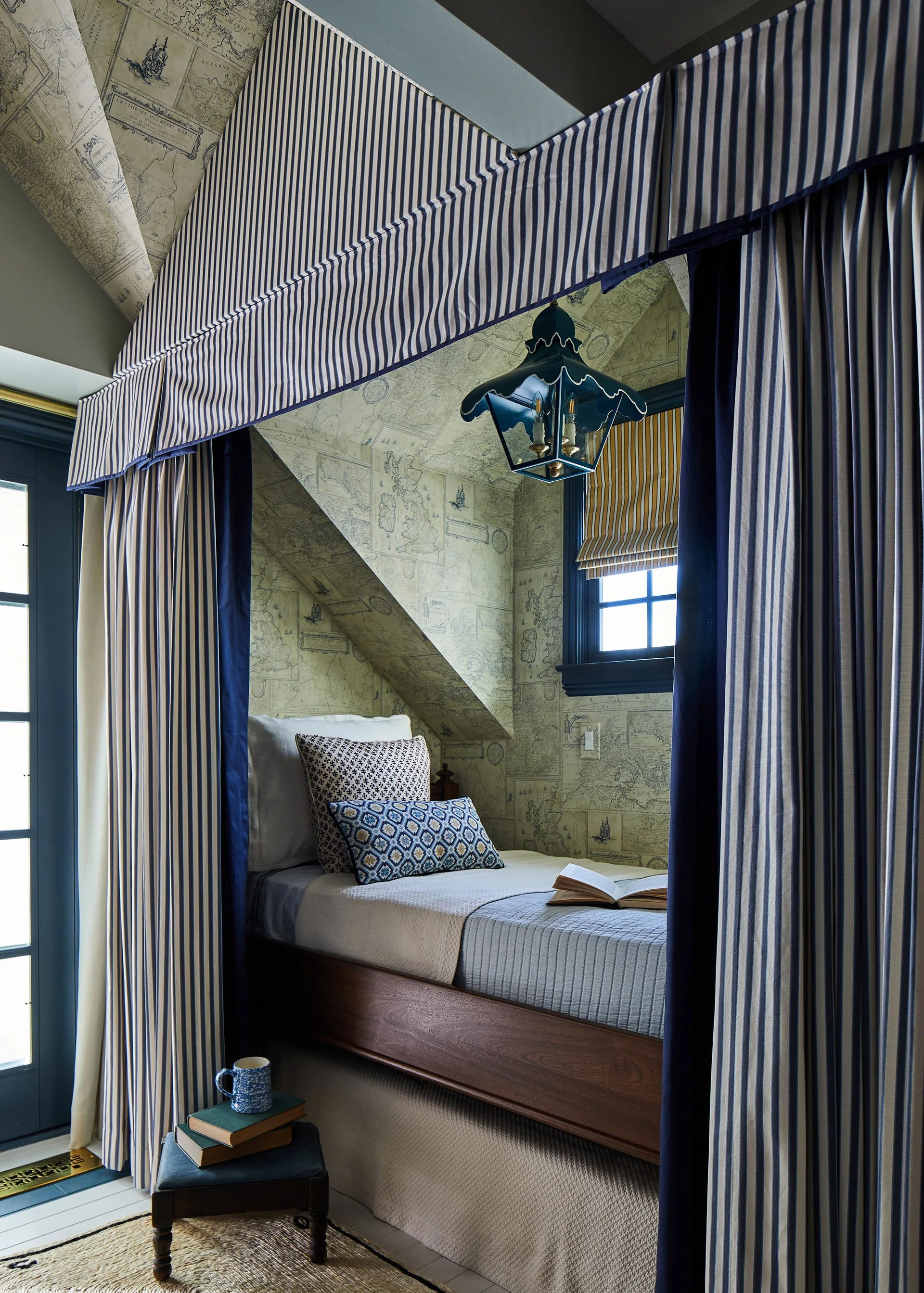A built-in wooden bed sits inside an alcove featuring antique map wallpaper, a blue and white striped fabric canopy, and a hanging blue lantern.