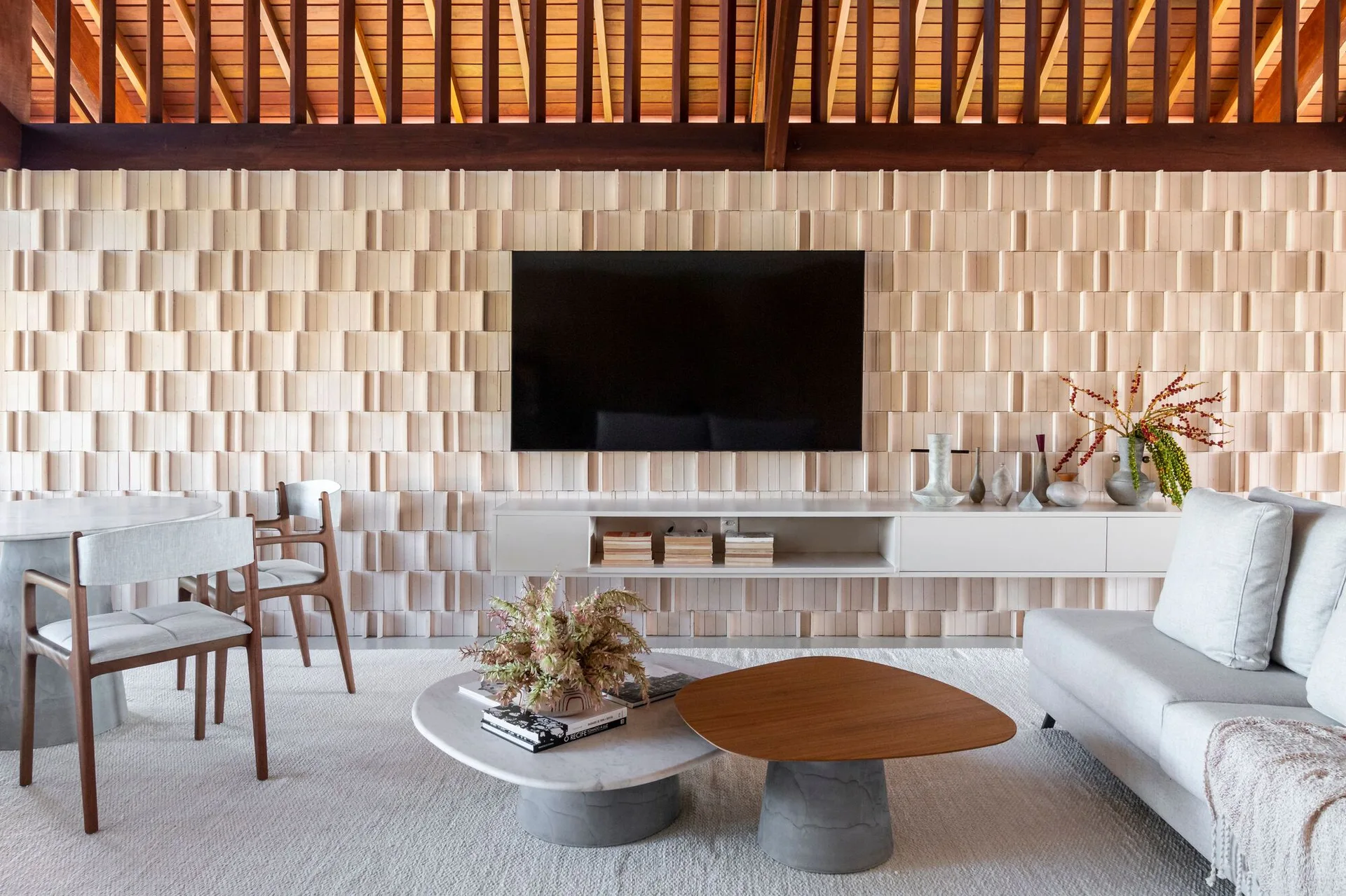 A contemporary living room features a textured wood block accent wall, a wall-mounted TV over a white floating console, and overlapping coffee tables.