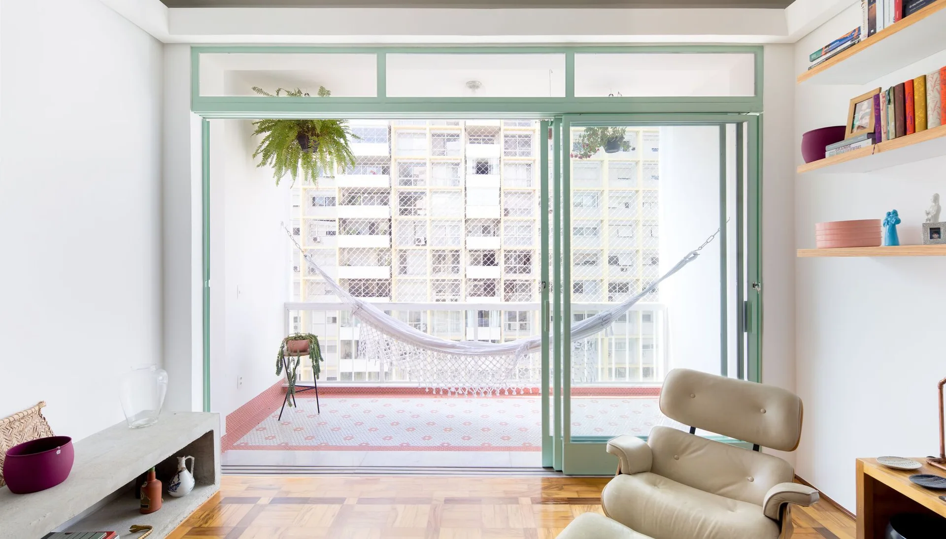 A bright living room with a leather lounge chair opens through mint green sliding doors to a balcony with a white hammock.
