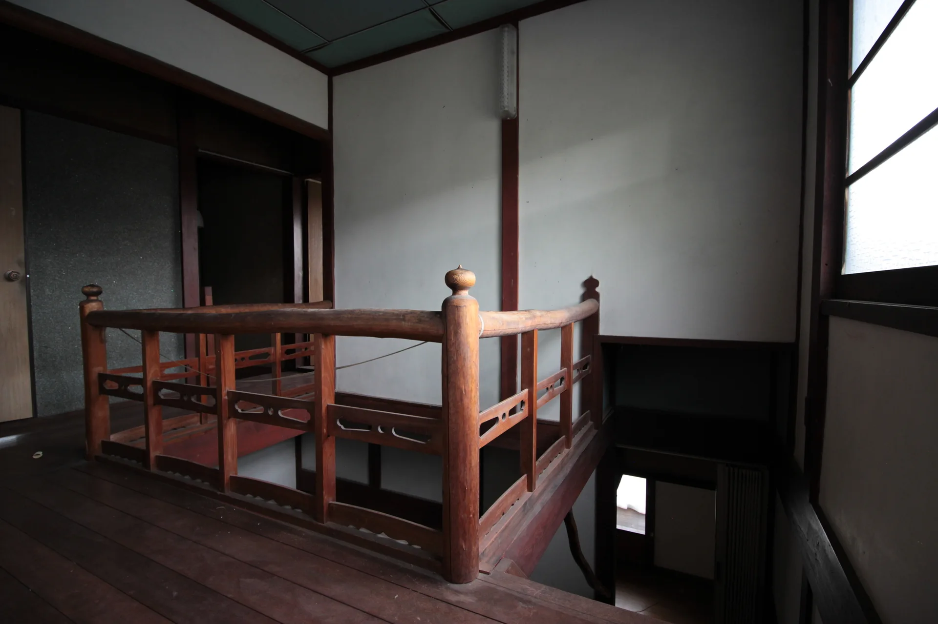 A dark wood mezzanine railing overlooks a staircase landing in a room with white walls, dark structural trim, and a window.