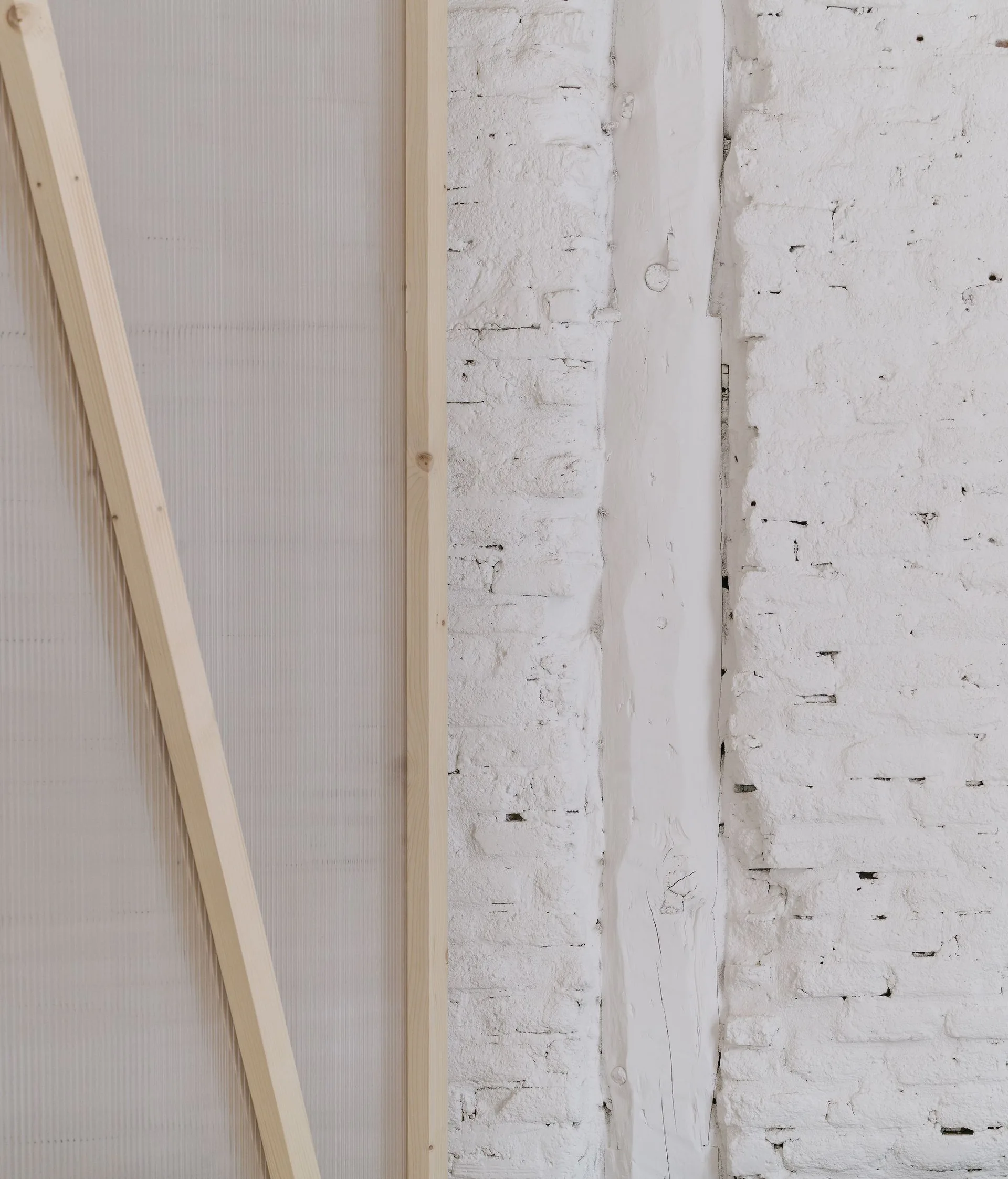 A close-up of a white painted brick wall with an embedded timber post next to a light natural wood frame containing a translucent ribbed panel.