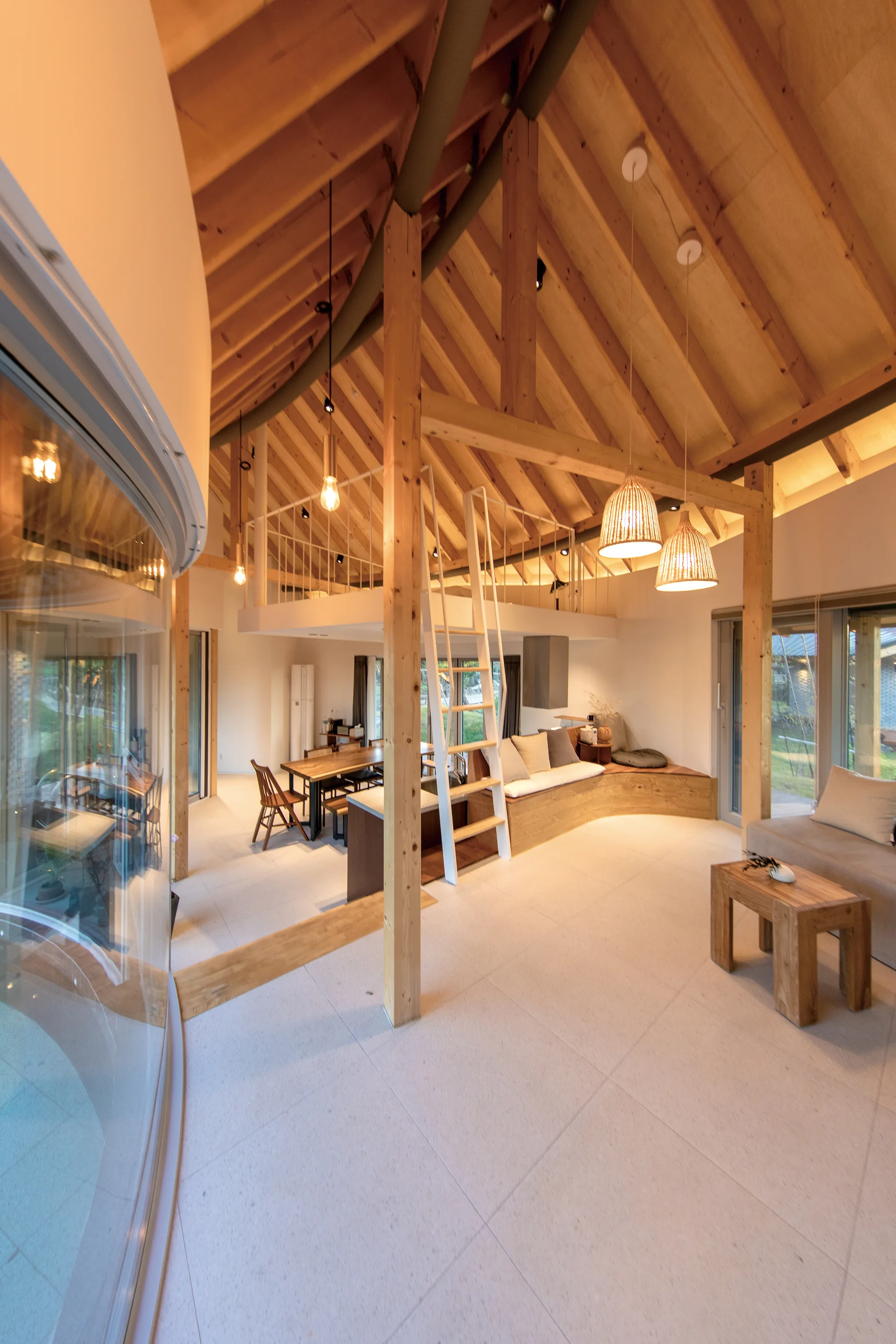 An open-plan living room features a dramatic vaulted timber ceiling, a white ladder leading to a mezzanine loft, and a curved built-in wooden bench.