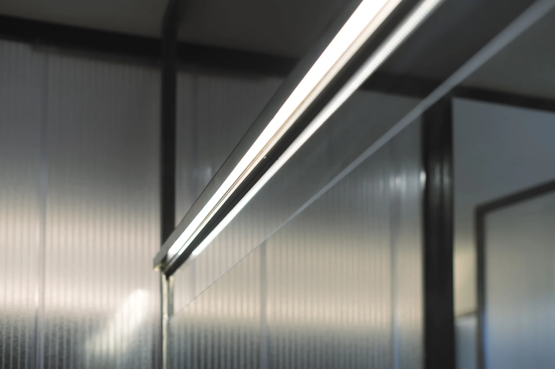 A close-up view of a bright linear LED lighting fixture mounted on a translucent fluted glass panel with a black metal frame.