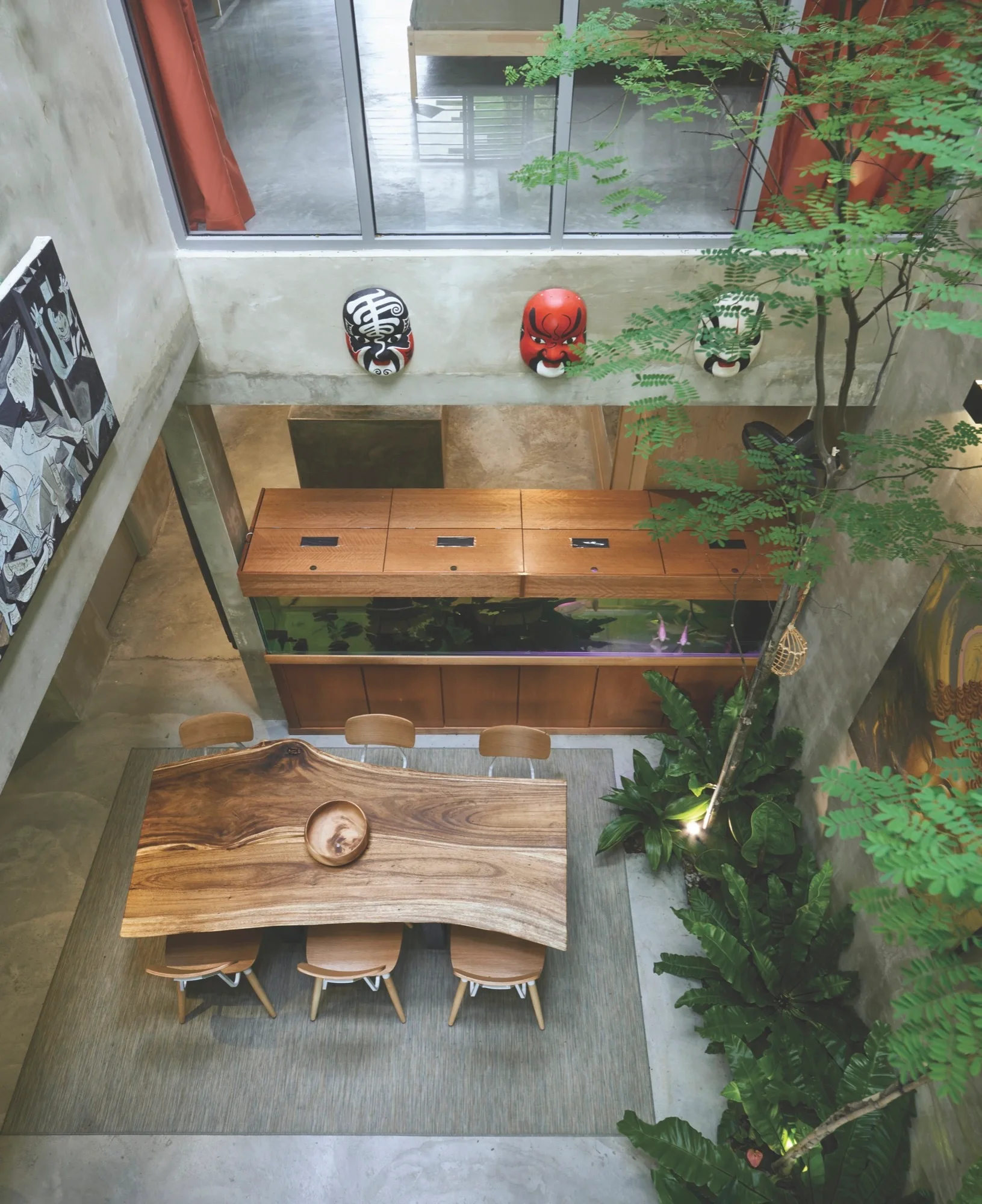 An overhead view of a dining room featuring a live-edge wooden table, matching chairs, an indoor tree, and a large wooden-framed aquarium.