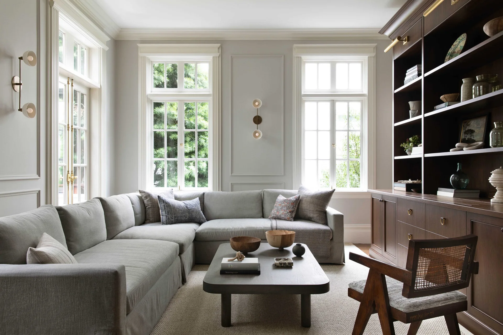 A transitional living room featuring a large gray sectional sofa, a dark wood built-in bookcase, a wooden coffee table, and walls with decorative molding.