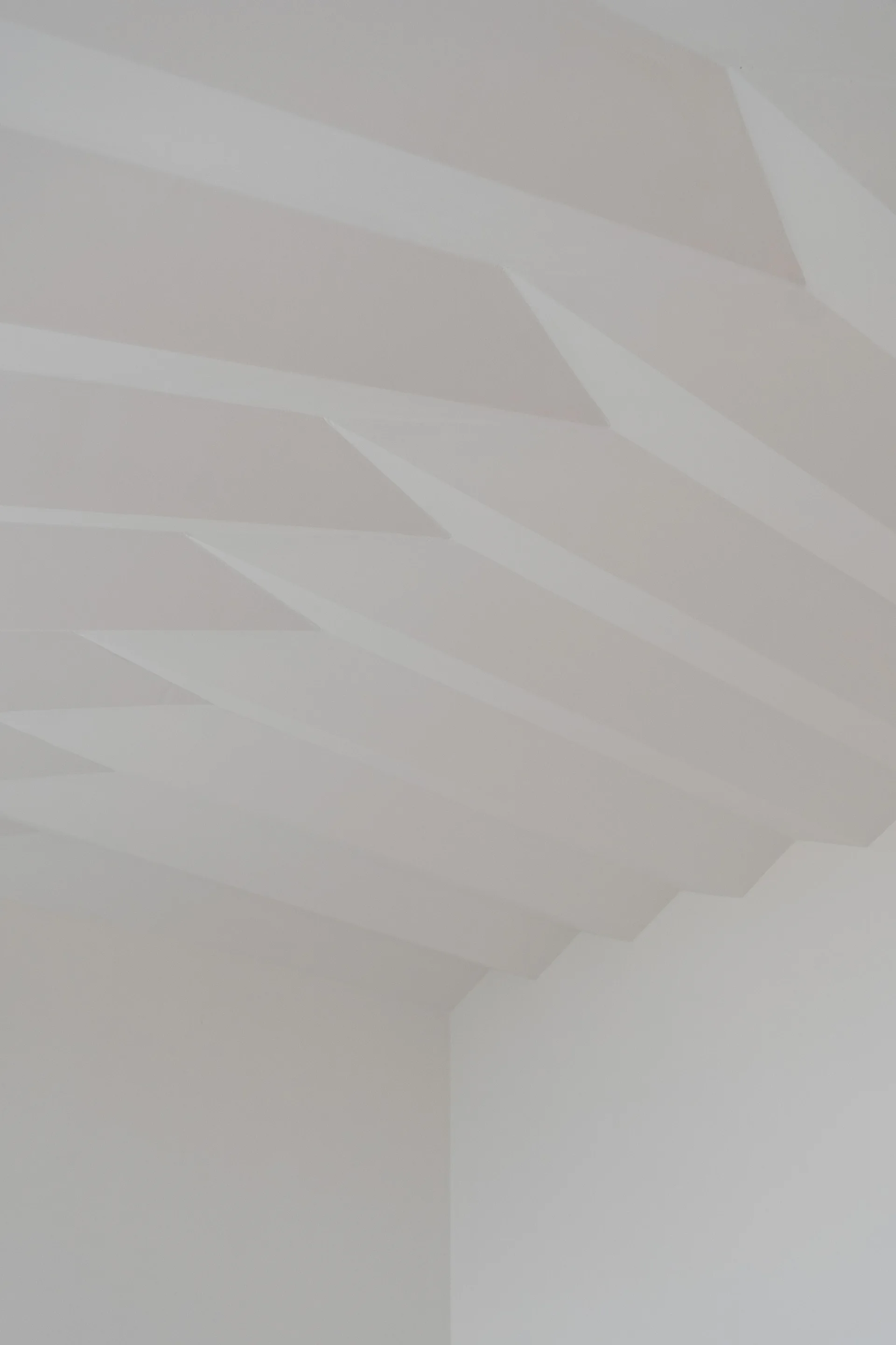 A minimalist white plaster ceiling with a stepped geometric pattern meets a plain corner wall under soft light.